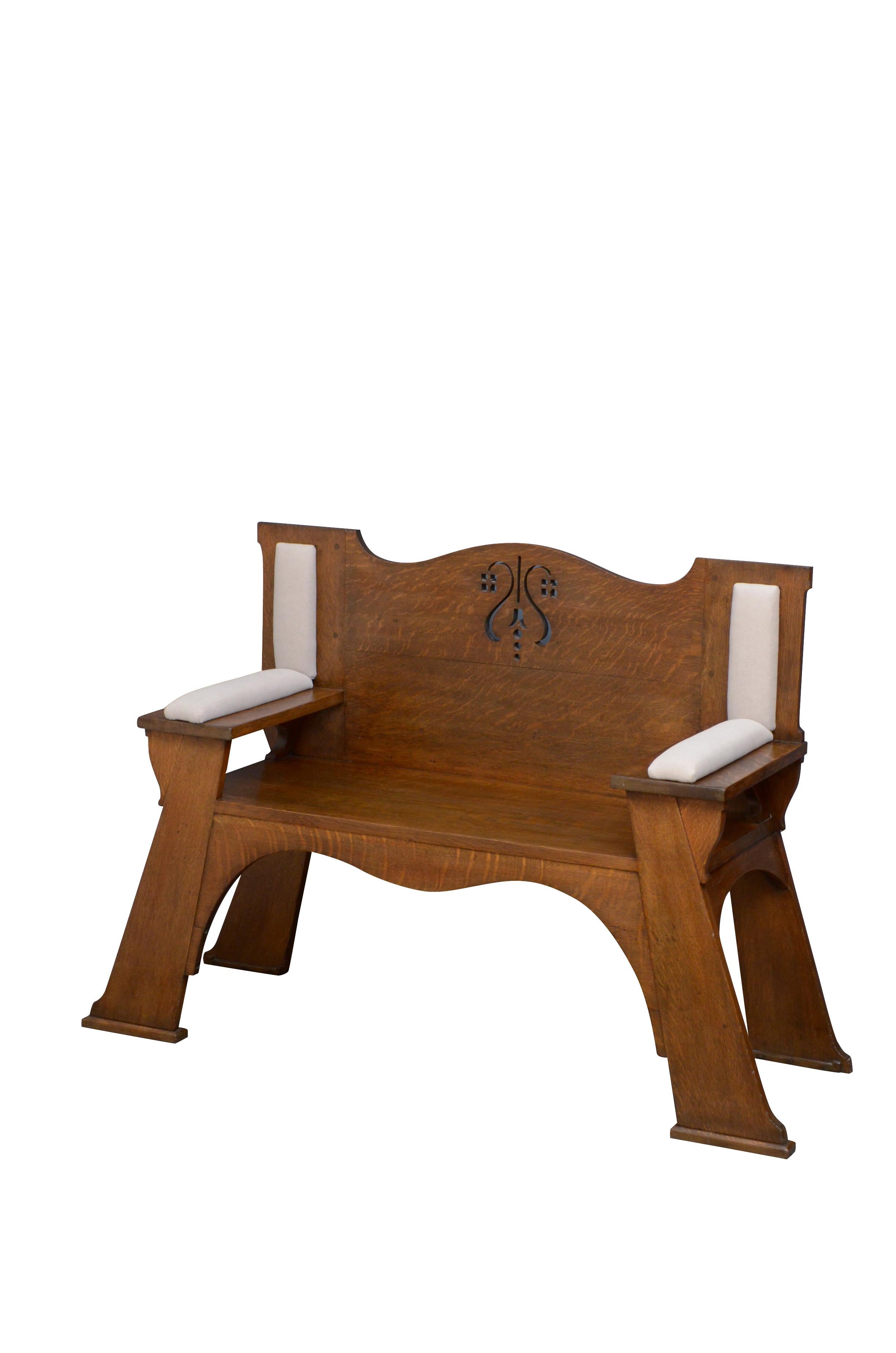 Substantial Arts & Crafts solid oak hall seat, having shaped and carved back and generous seat flanked by padded arms, all standing on outswept legs united by shaped apron. This antique bench retains its original finish, color and good patina, all