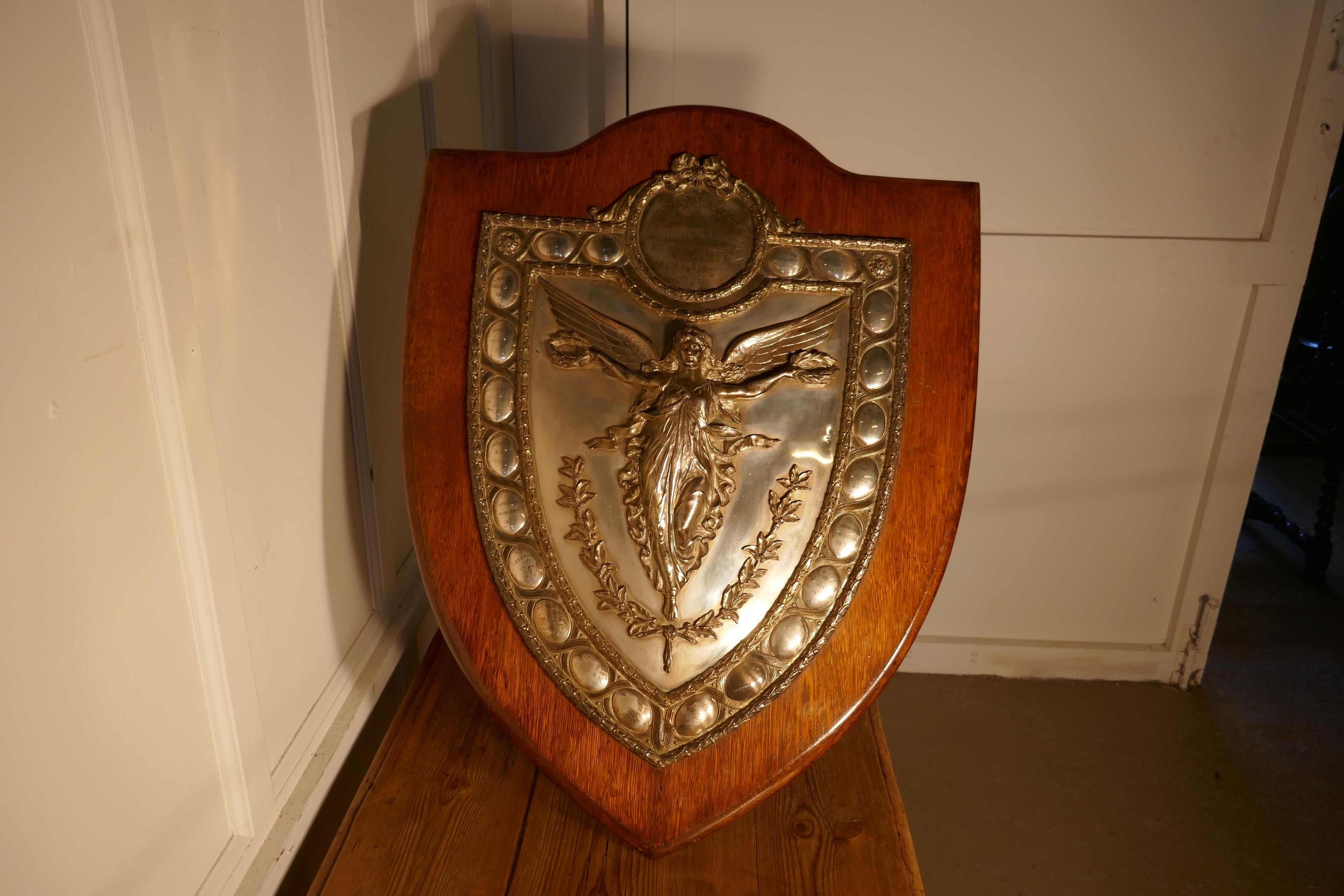 Large Arts and Crafts Shield Trophy with Nike the Goddess of Victory 

The is a very impressive Arts and Crafts piece, the Golden Oak shield has a large silver plated mount, in the centre there Nike the Winged Greek Goddess of Victory celebrating