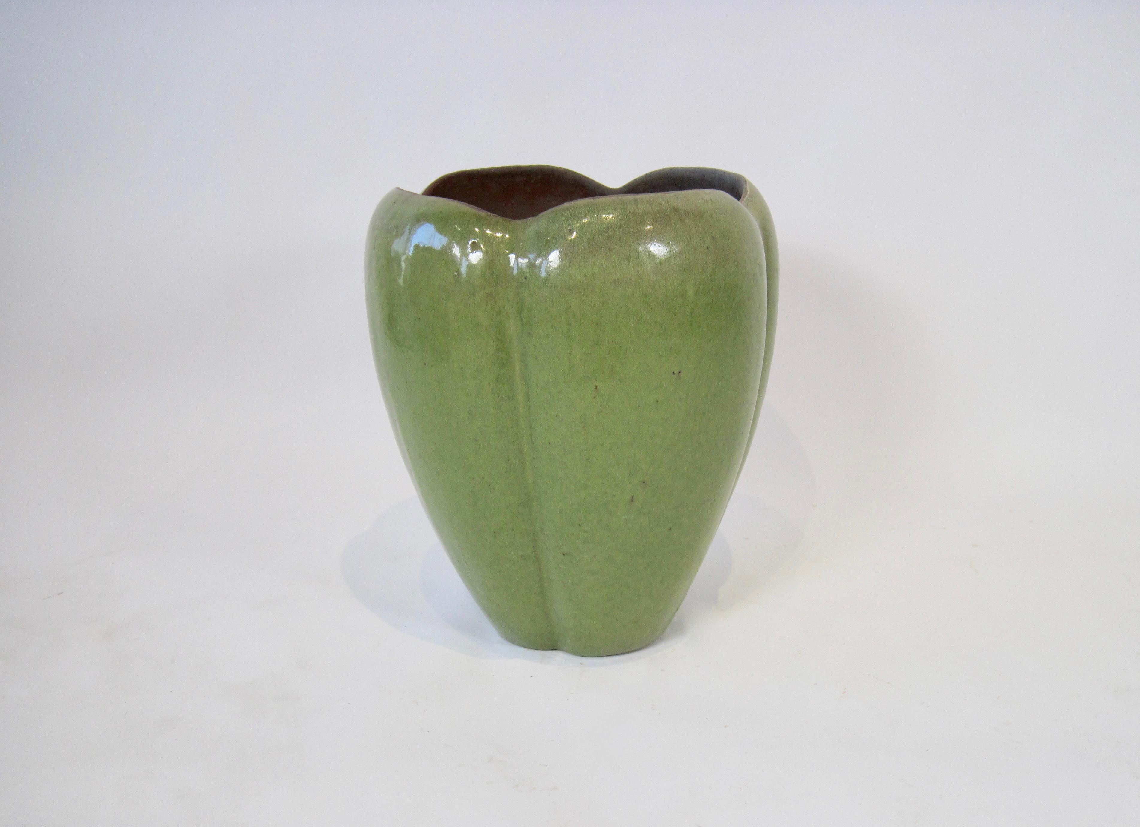 An arts & crafts style flower bud earthenware jardinière. Four green glazed petal like sections widen upwards and curve slightly inward at the top. This planter is substantial in weight and form.