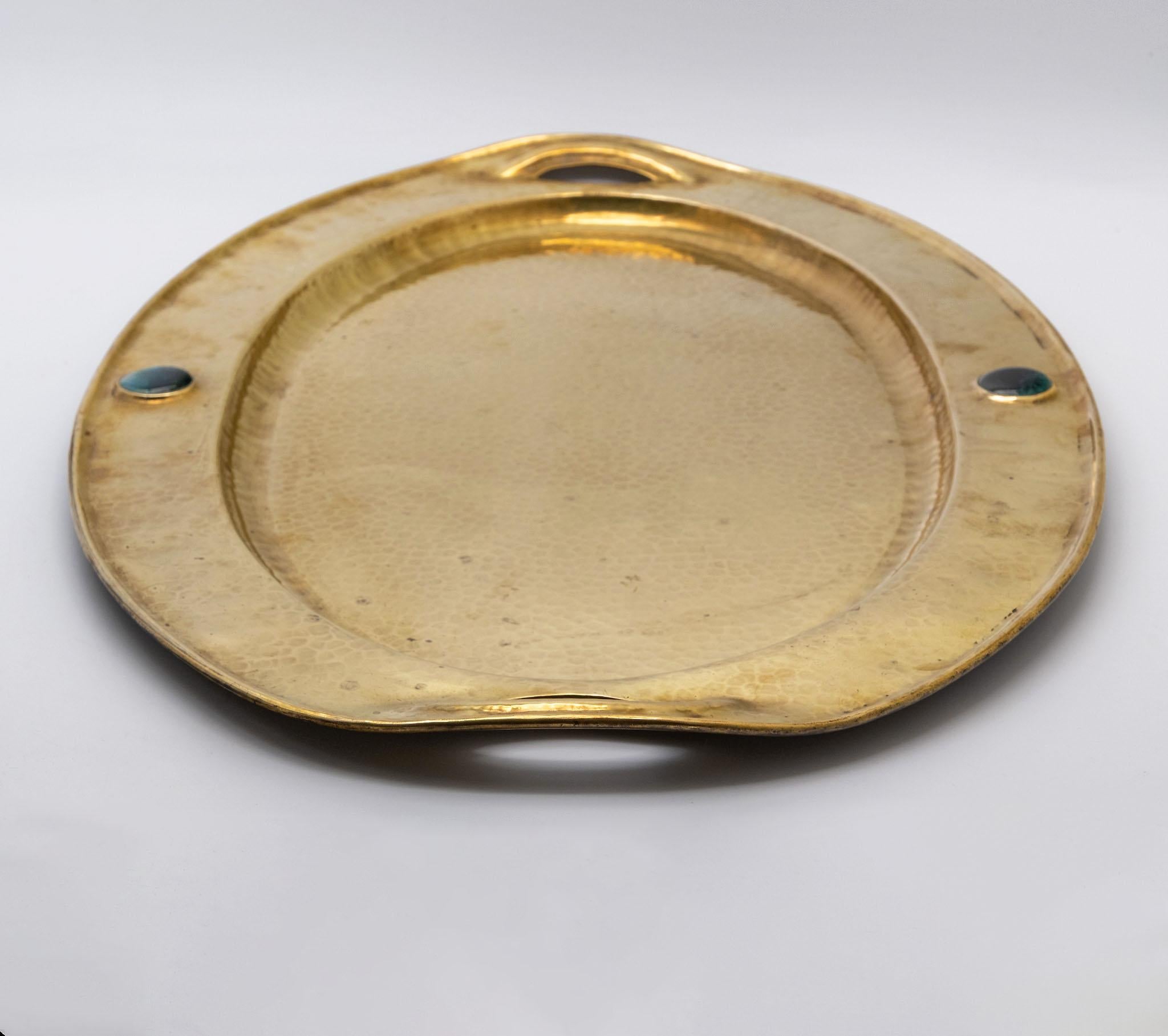 Grande vassoio in ottone battuto Arts & Crafts con due tondi cabochon.  Circa 1900.

Il vassoio è stato lucidato nel corso degli anni e presenta differenze di colore che gli conferiscono un fascino vintage. Il vassoio è piatto e presenta alcuni