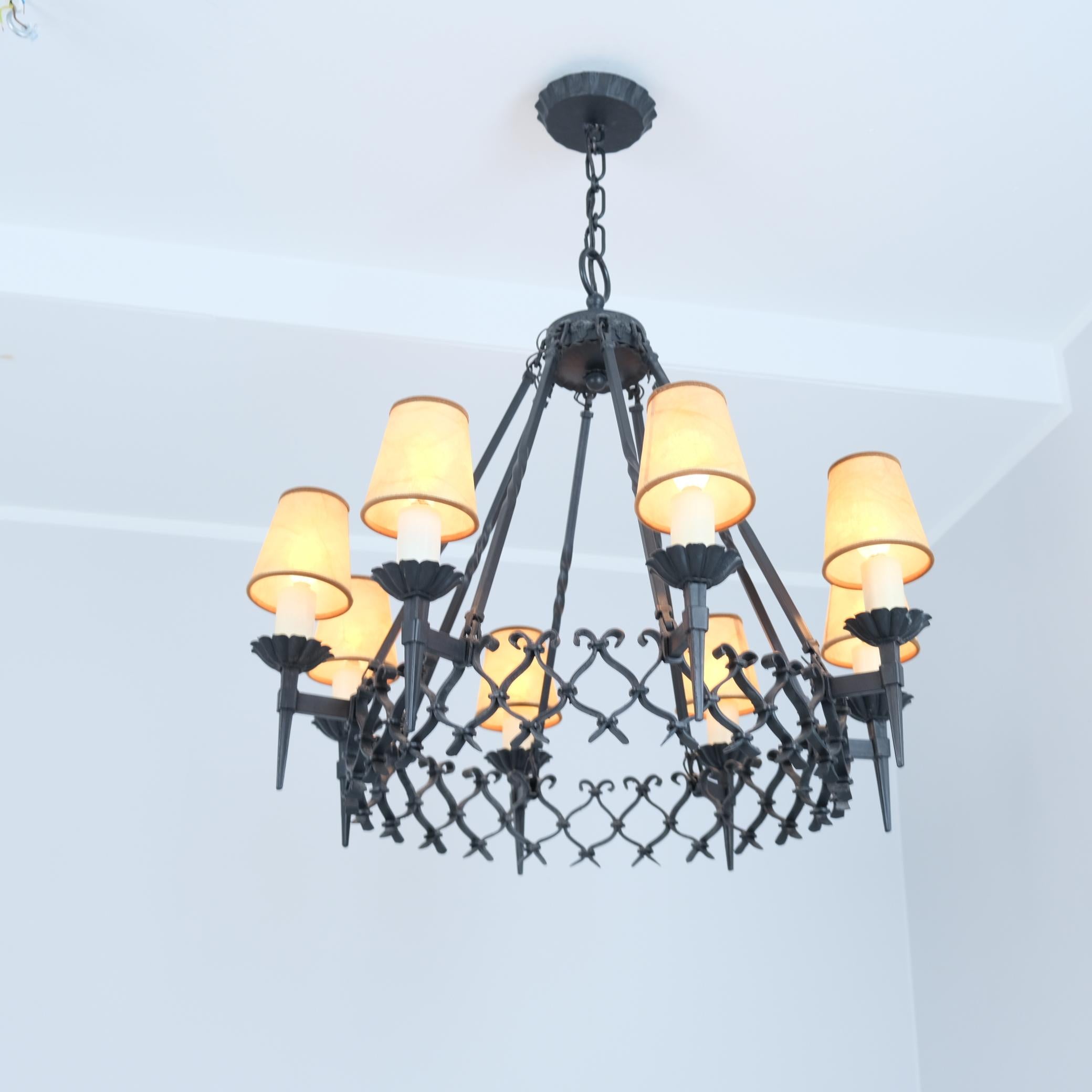 Una gran lámpara finlandesa de hierro forjado con hermosas colas. La lámpara mide 75 cm de diámetro con las pantallas, y presenta 8 luces que sobresalen de un anillo central con un intrincado diseño de malla. La lámpara está pintada de negro y es