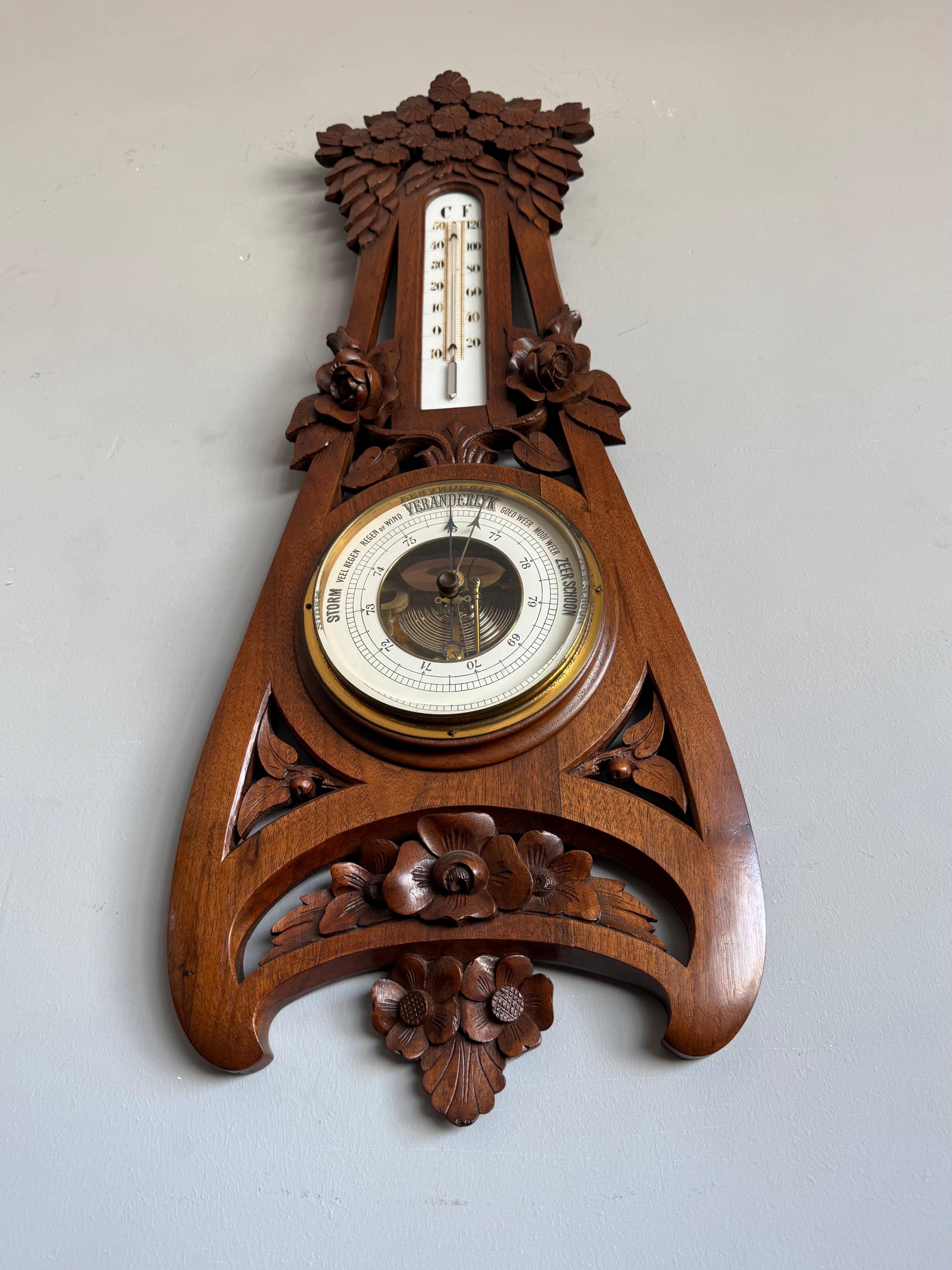 This rare and decorative early 20th-century Arts & Crafts wall barometer and thermometer is a striking testament to Dutch craftsmanship. Hand-carved from a single solid piece of richly patinated nutwood, the piece is adorned with deeply sculpted