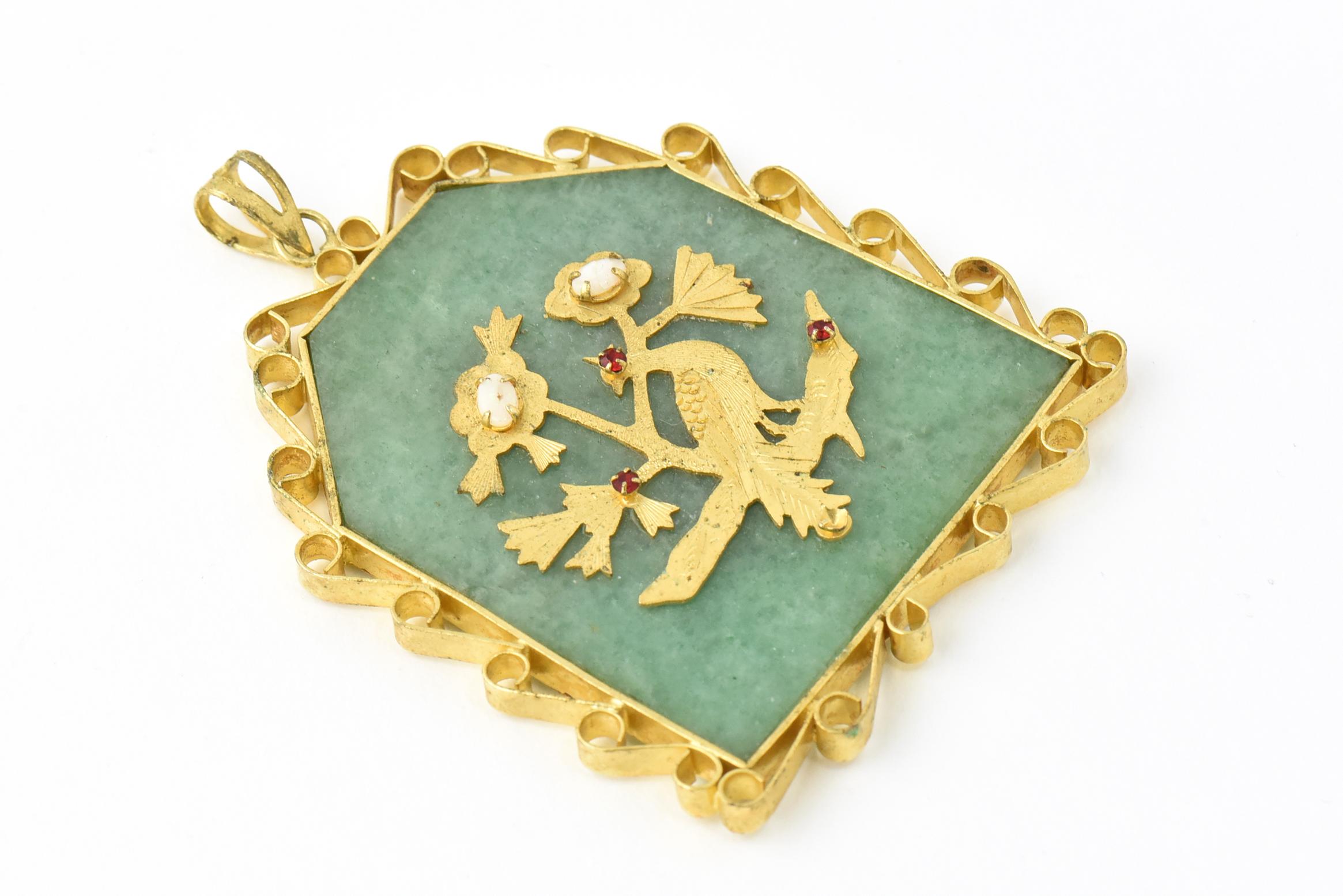 Asian-motif gold-plated pendant with scroll edges, dating from the 1950s to 1960s. One side features a Asian symbol and the other side has a bird sitting on a branch with opal flowers and faux-ruby accents. Age wear, tarnished, crack in opal.
