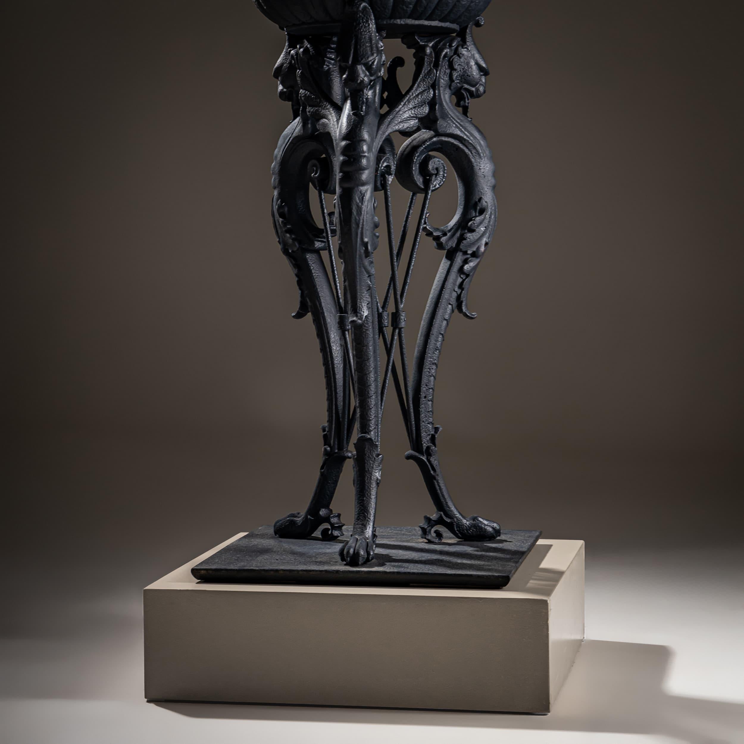 Large Athénienne crafted from iron with a black patina, supported by three legs terminating in winged lion heads. Resting atop is a basin with gadrooned sides, a domed lid, and three handles. This tripod-style design, executed in classical taste,