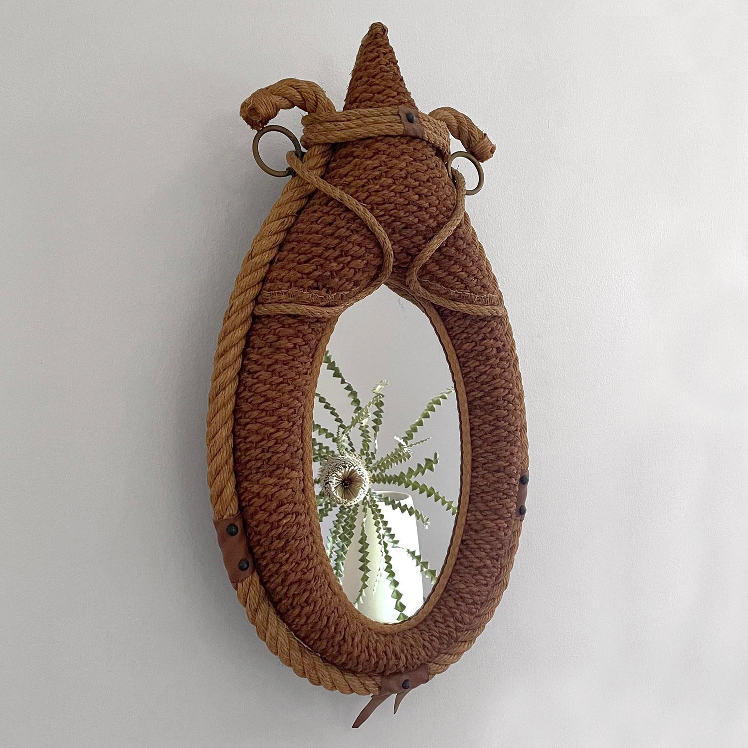 Adrien Audoux & Frida Minet rope wall mirror
France, circa 1950’s
Original oval shaped mirror has light fogging 
Mirror frame comprised of signature braided rope
Accented with a variety of adornments and aged leather banding with stud rivet