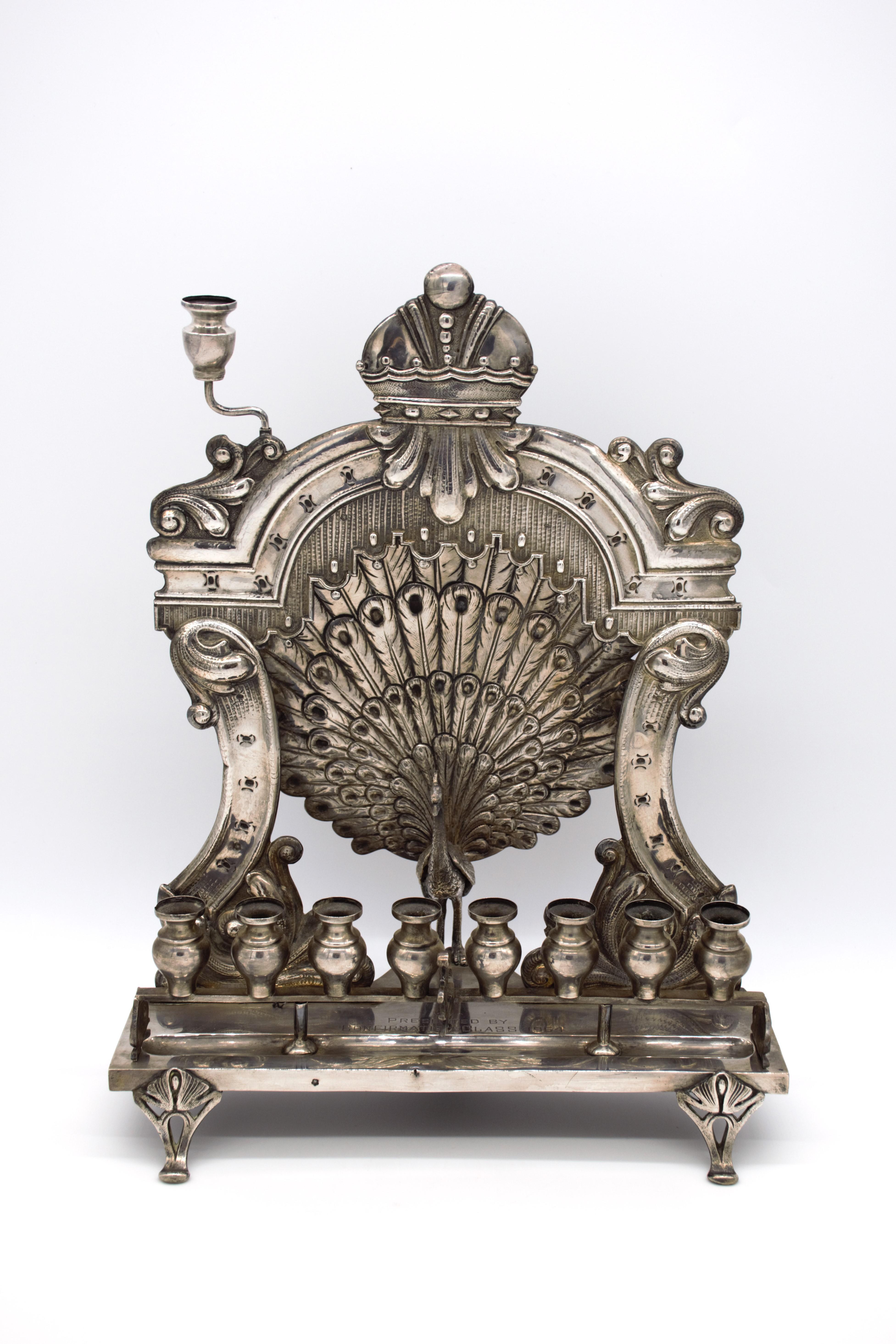 Très rare et important objet en argent autrichien, datant de l'âge d'or de la fin du 19e siècle et du début du 20e siècle, cette lampe de Hanoukka est ornée à la main d'un proscenium drapé ciselé renfermant un paon en exposition, précédé d'un