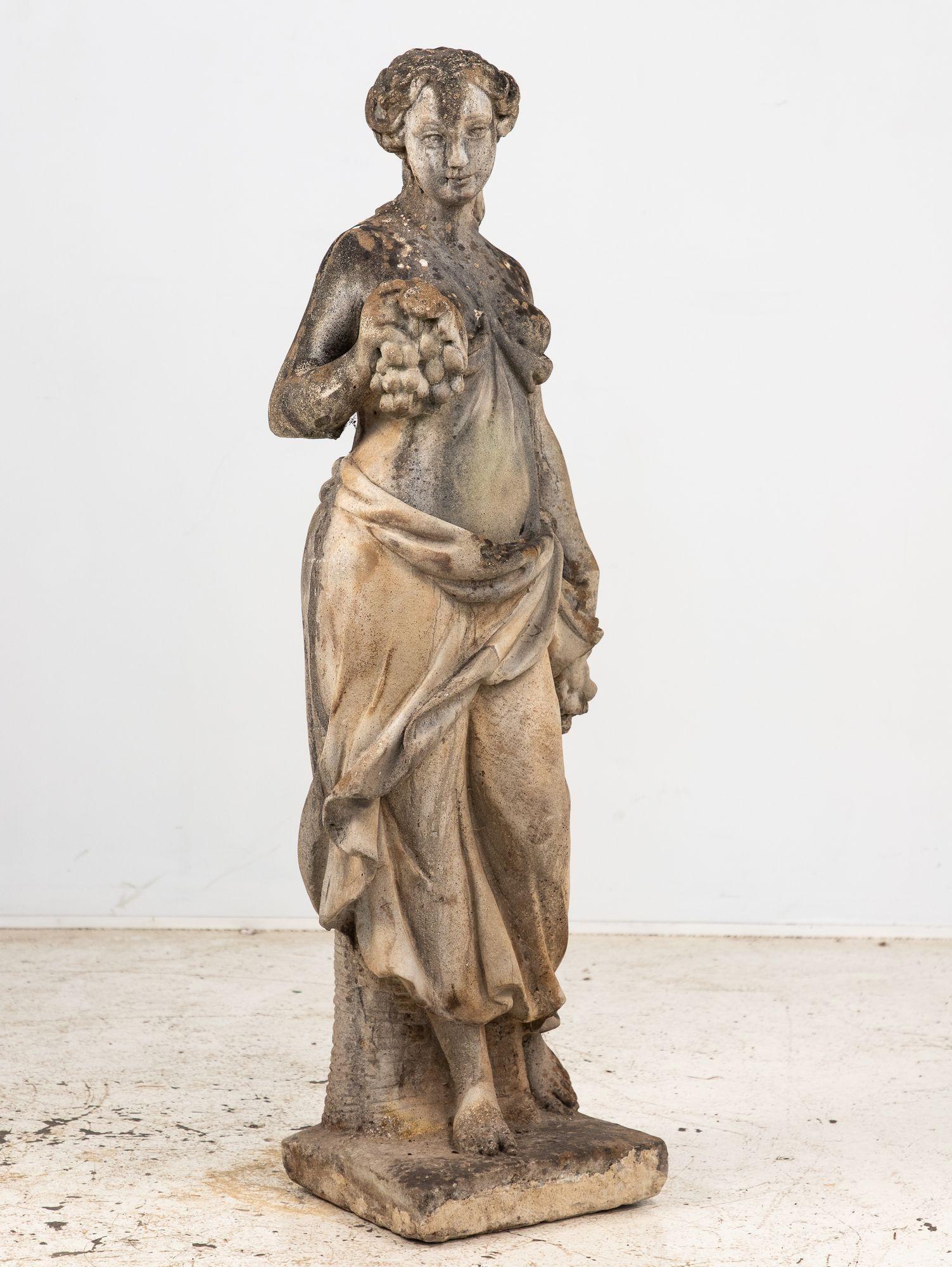 Fangen Sie die Essenz der Erntezeit mit dieser beeindruckenden Gartenstatue der Göttin des Herbstes aus Beton ein. Elegant in ein fließendes Gewand gehüllt, hält sie großzügige Trauben in der Hand - eine Hand als Opfergabe erhoben, die andere