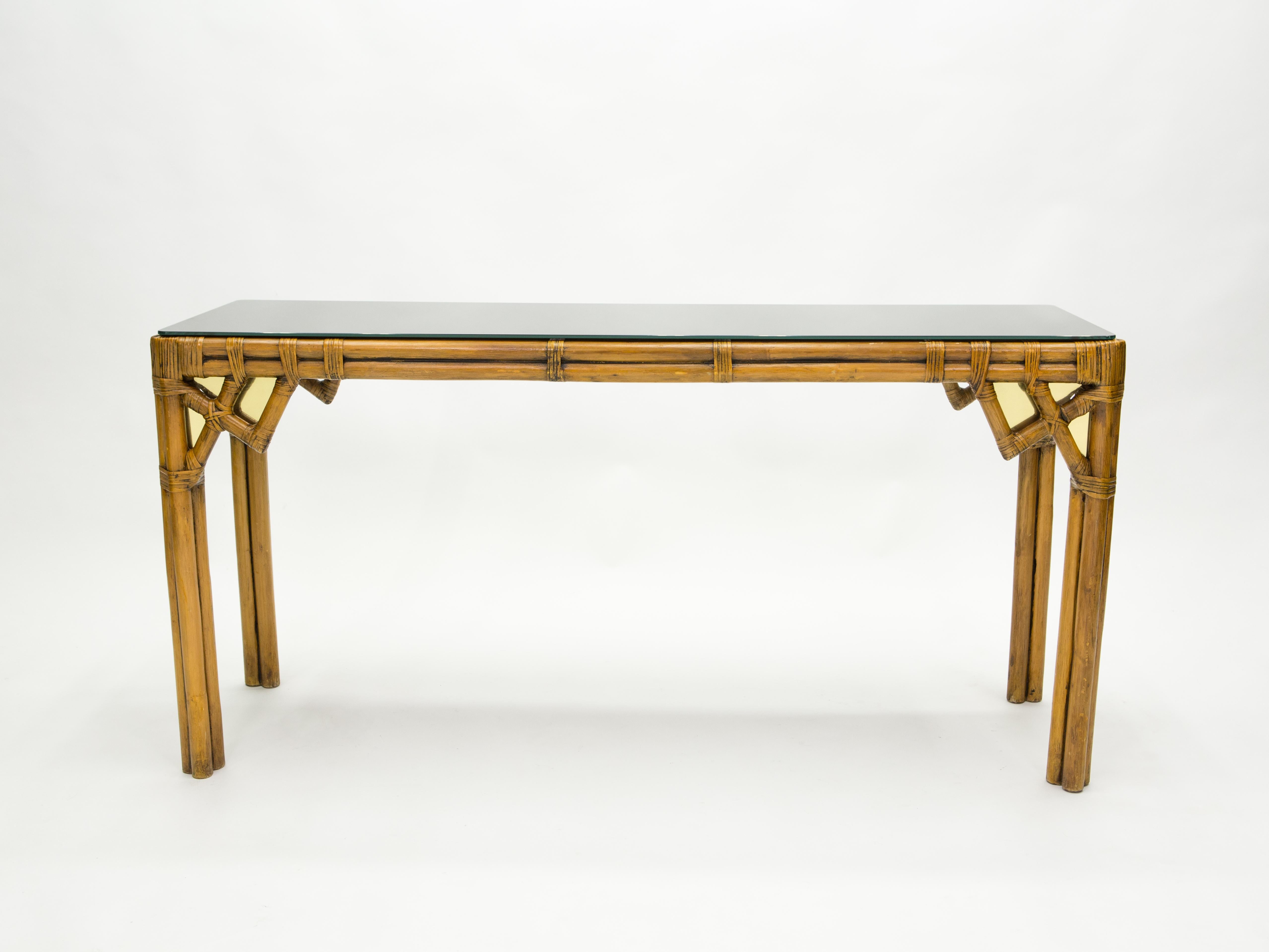 This beautiful console table was made from natural bamboo, with cane joints and luxe displays of brass inserts on the front and side, in the early 1970s in Italy. It features a slick black opaline glass top. The piece was designed from the