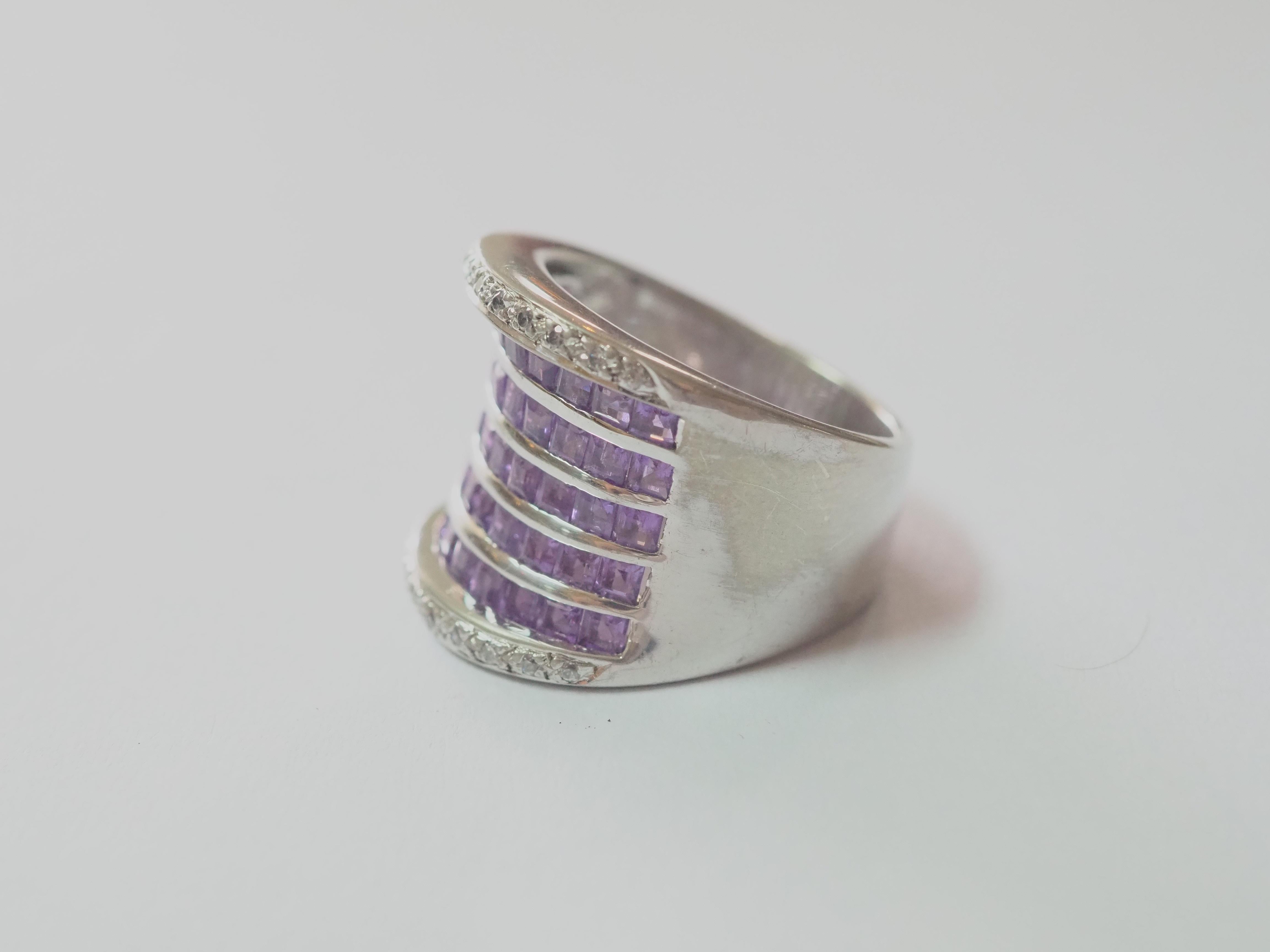 Dieser Ring ist ein schöner Bandring aus massivem Sterlingsilber. Der Ring ist mit natürlichen violetten Amethysten verziert, die in 5 sich überschneidenden Linien kanalisiert sind. Die weißen Steine an beiden Enden sind Cubic Zirconia. Der Amethyst
