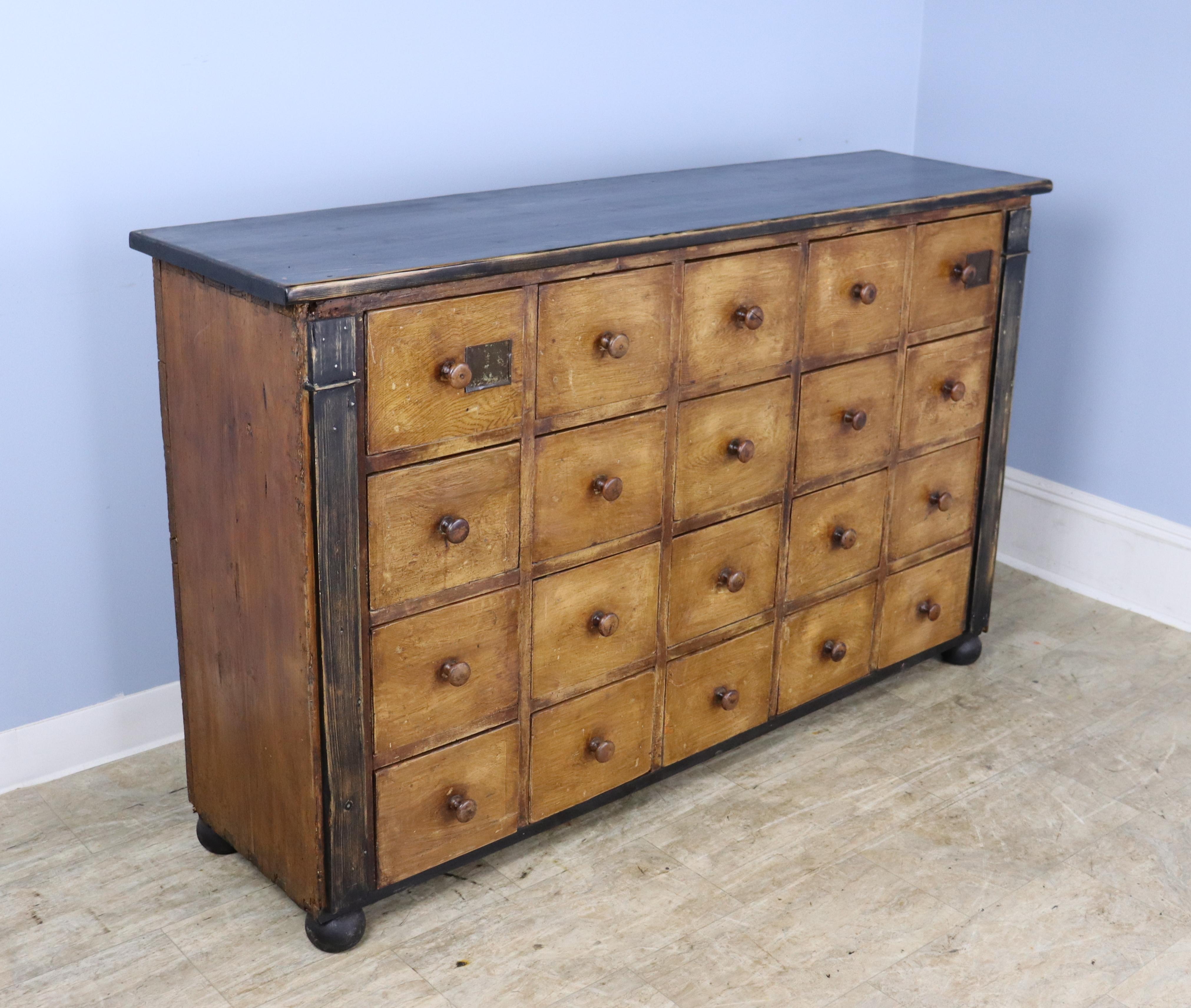 An imposing flight of 20 drawers, just the right depth and length to act as an interesting storage and case piece. The top is new and faux distressed. The paint on the drawers is original, and there are remnants of the old colored powders that were