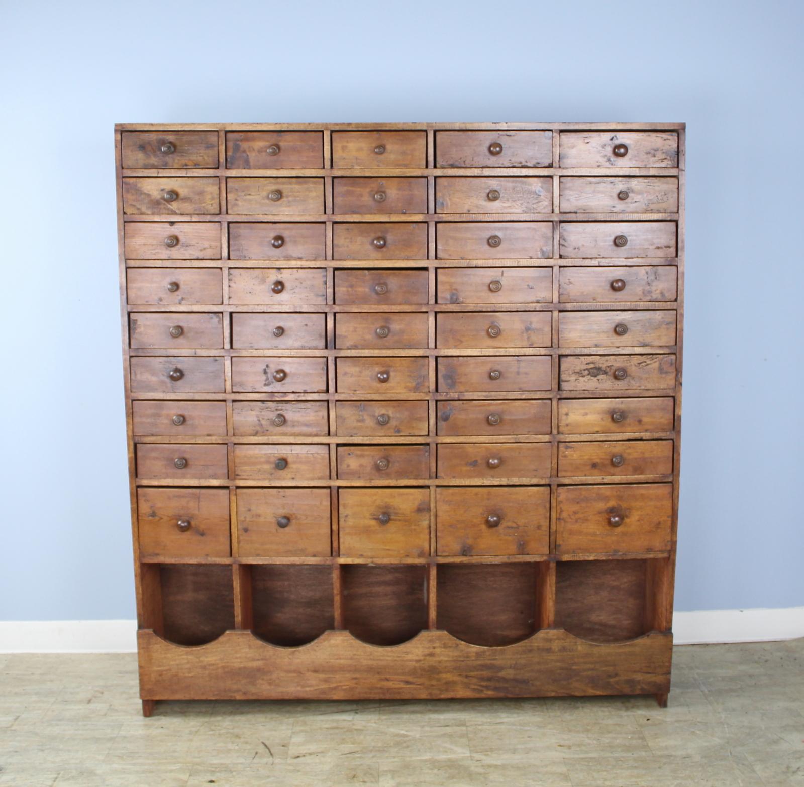 A large bank of drawers in rustic pine. Imposing and charming at the same time. The drawers are hand wrought and have mismatched knobs. The original red stain has been rubbed back and the piece has been newly stained and waxed for excellent shine