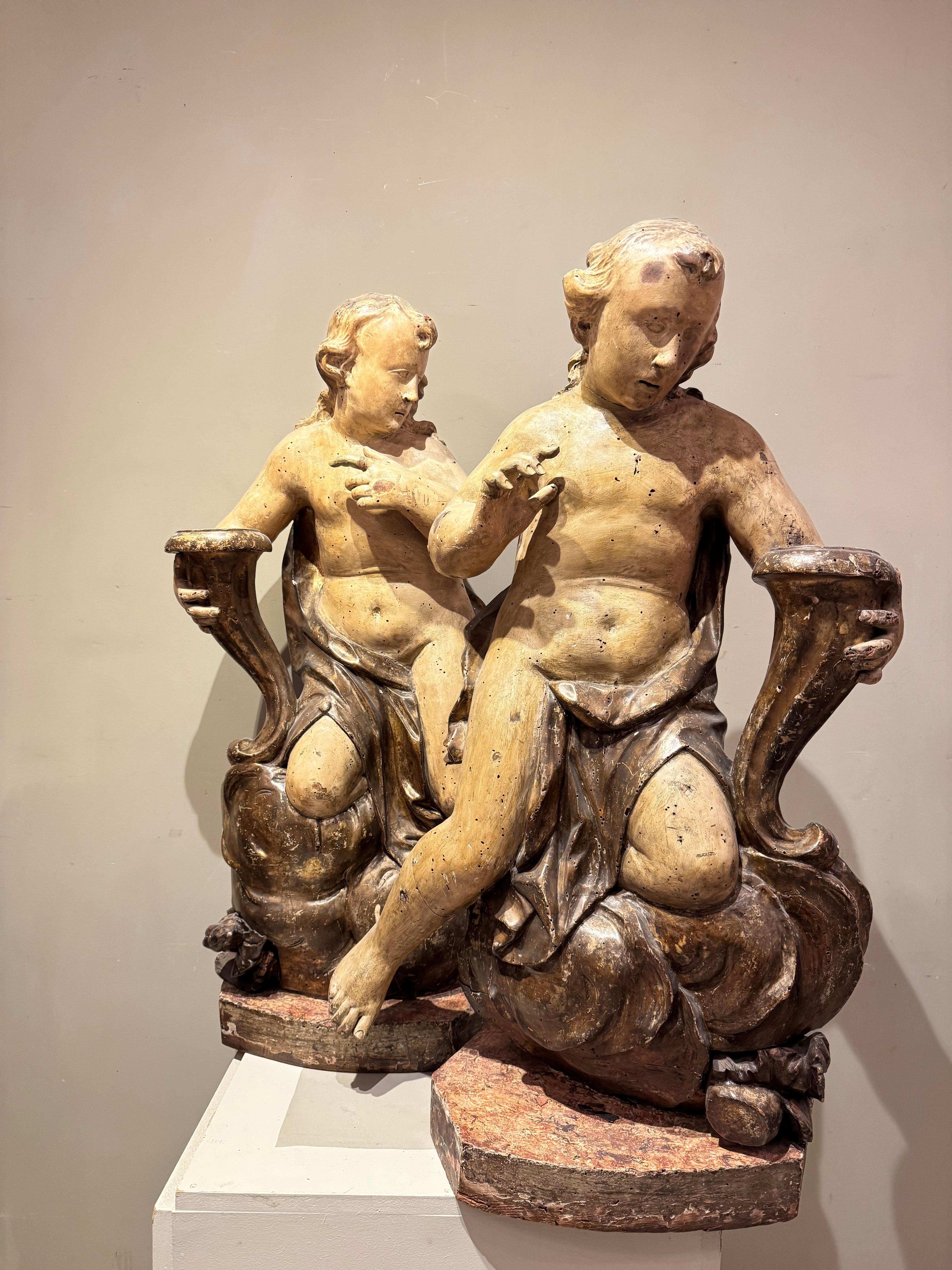 Zwei große, rund geschnitzte Statuen, die wahrscheinlich ceruleanfarbene Engel darstellen (obwohl es keine Hinweise auf Flügel auf der Rückseite gibt) oder Allegorien des Glücks (in diesem Fall können wir annehmen, dass sie Hörner des Überflusses