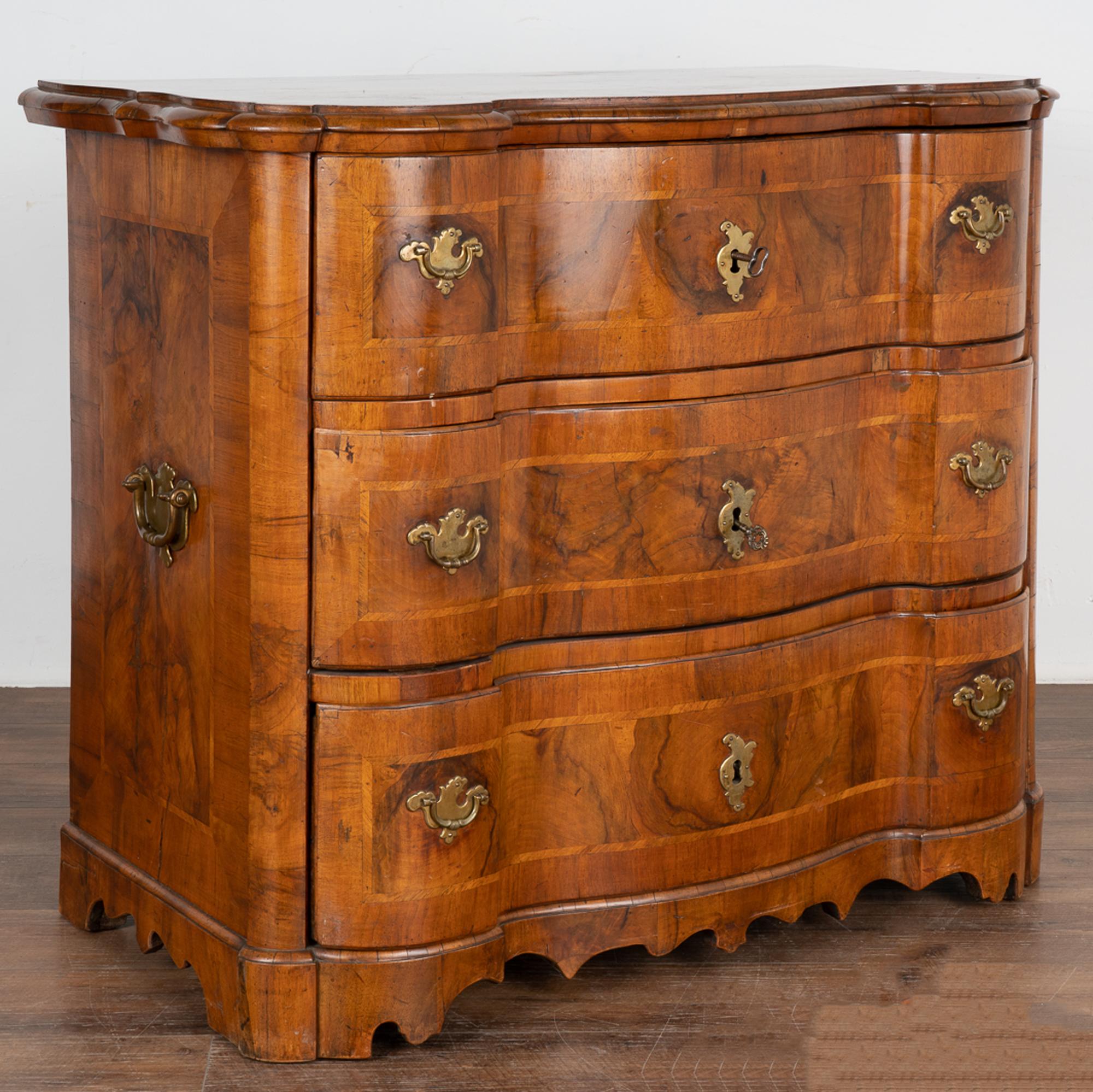 Large handsome baroque oak chest of drawers veneered with walnut and elm, curved front with three drawers.
Brass hardware including side handles, drawer pulls and keyhole covers.
Two brass pulls on each drawer; top drawer locks and opens with heavy