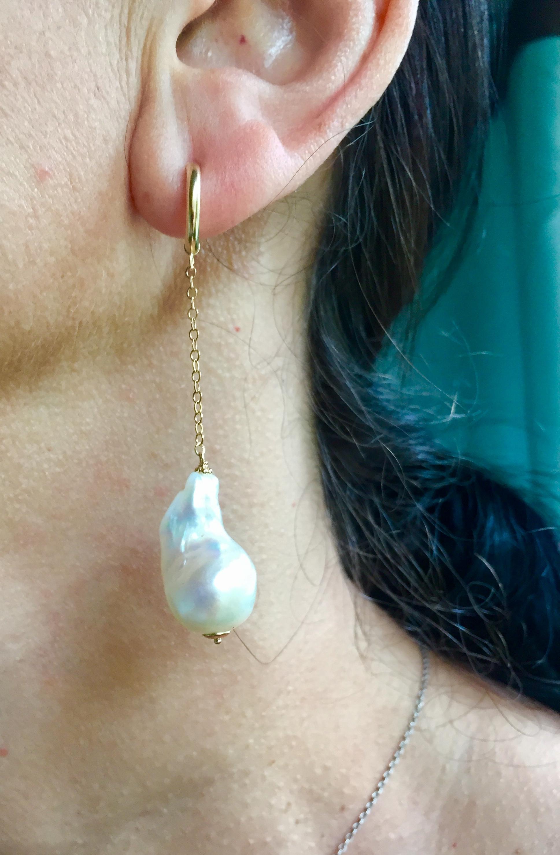 These large baroque white pearl dangle earrings with 14k yellow gold chains are stunning. The glowing white pearl is highlighted by an elegant 14k yellow gold chain and stud. These dangle earrings beautifully frame the face at 2.5 inches. The