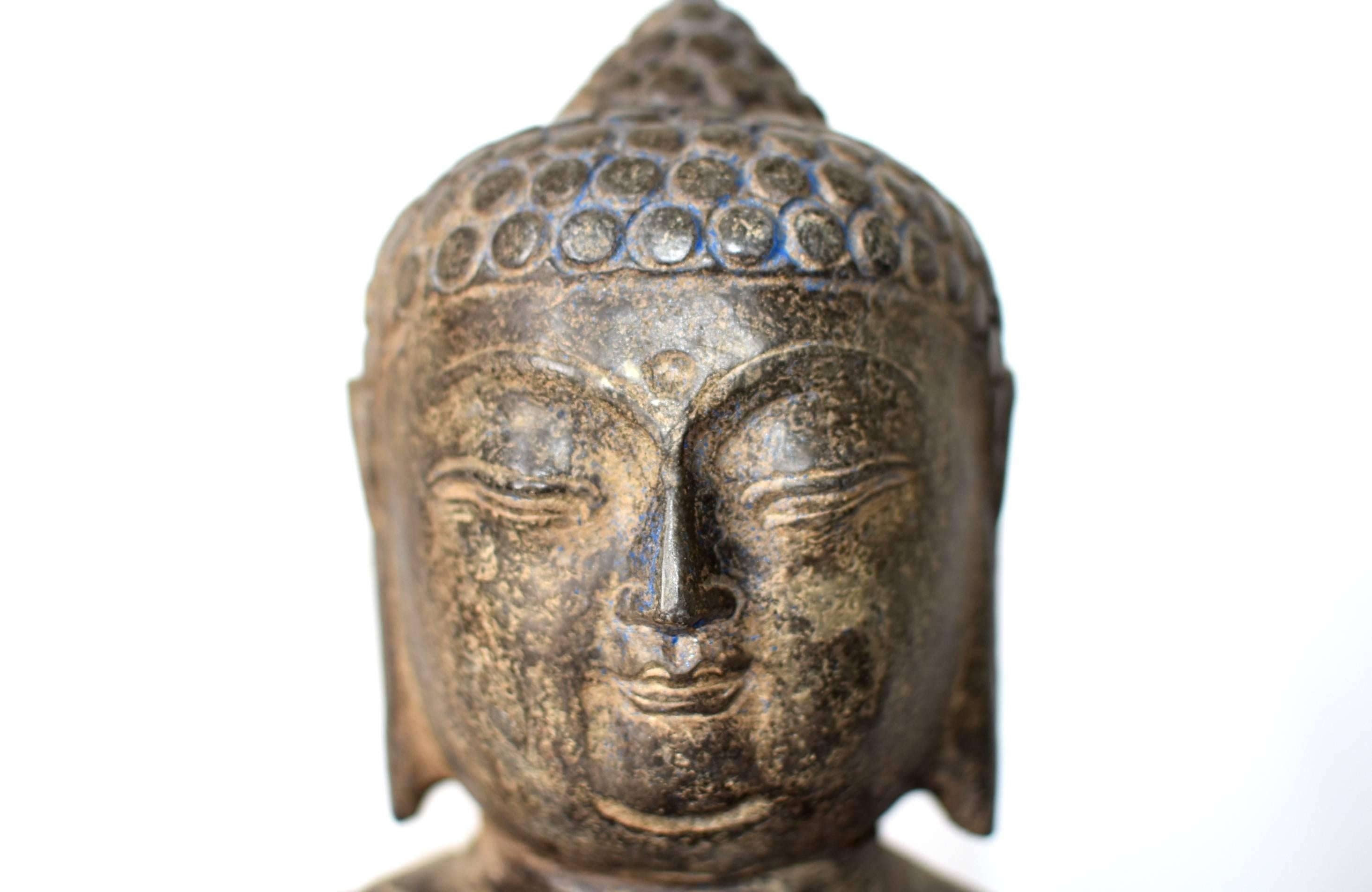 This is a large solid stone Buddha sculpture. The Buddha has a young, full face with swirled hair and long earlobes, all in Tang dynasty style. His expression is calm and peaceful. This hand carved sculpture depicts Buddha in a seating position,