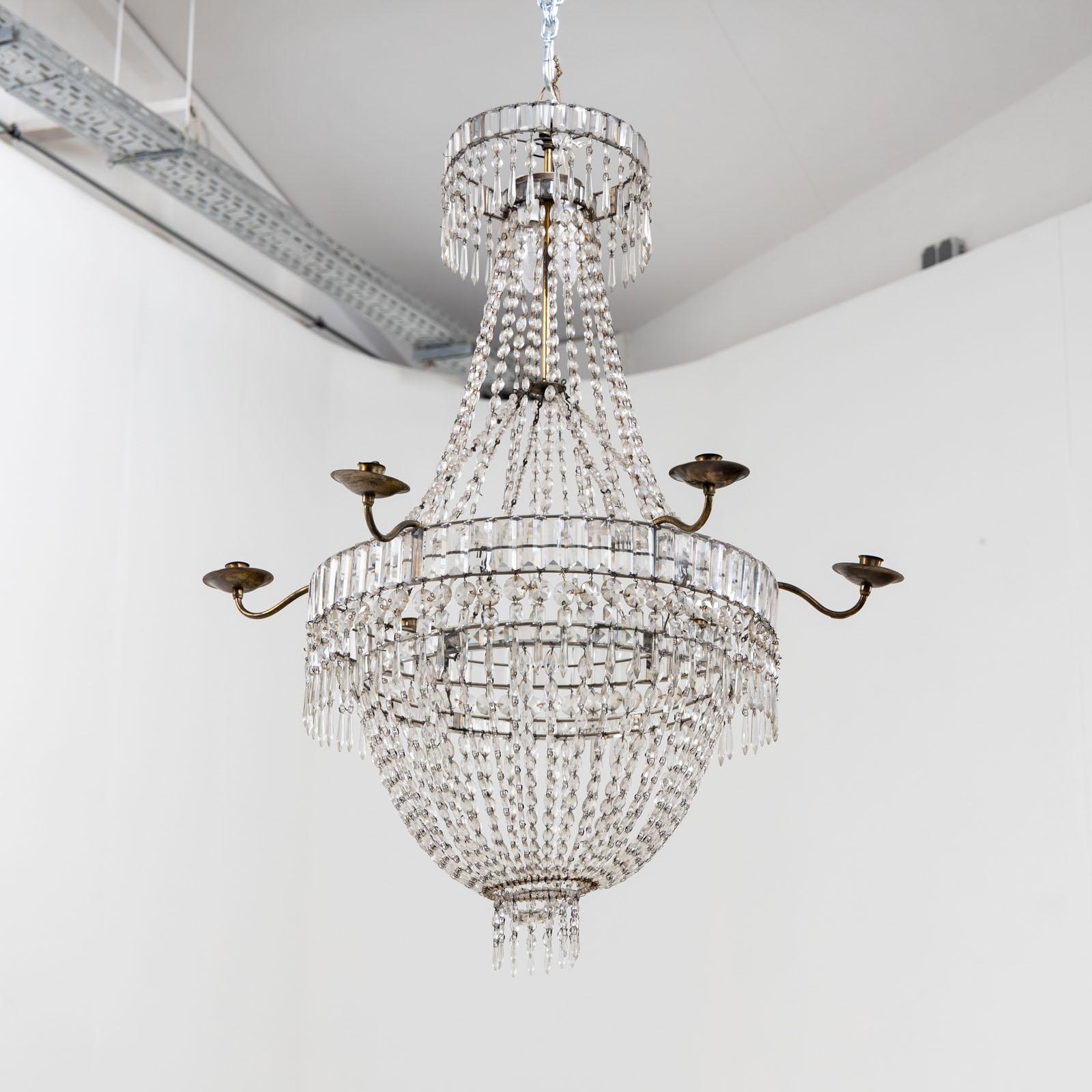 Large ceiling chandelier with six brass candle holders. The hanging of glass prisms, drops and beads is guided over two hoops and ends in a basket with hanging drops.