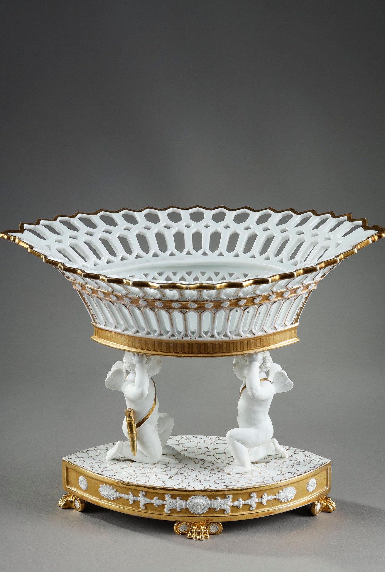 Very large navette-shaped basket in white openwork porcelain with gold highlights, resting on two kneeling cupids carrying their quivers, on a base of the same shape and standing on claw or lion's paw feet. The oblong base is decorated on both sides
