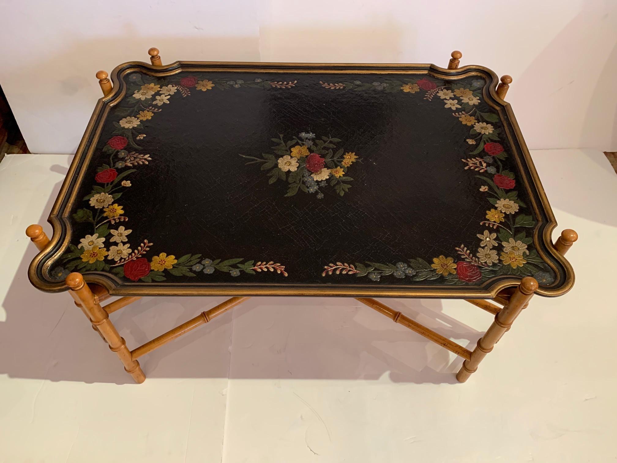 A big elegant rectangular tray top coffee table having embossed painted top with flowers on top of black background with slightly distressed surface. The top is nicely offset with a bamboo base.
