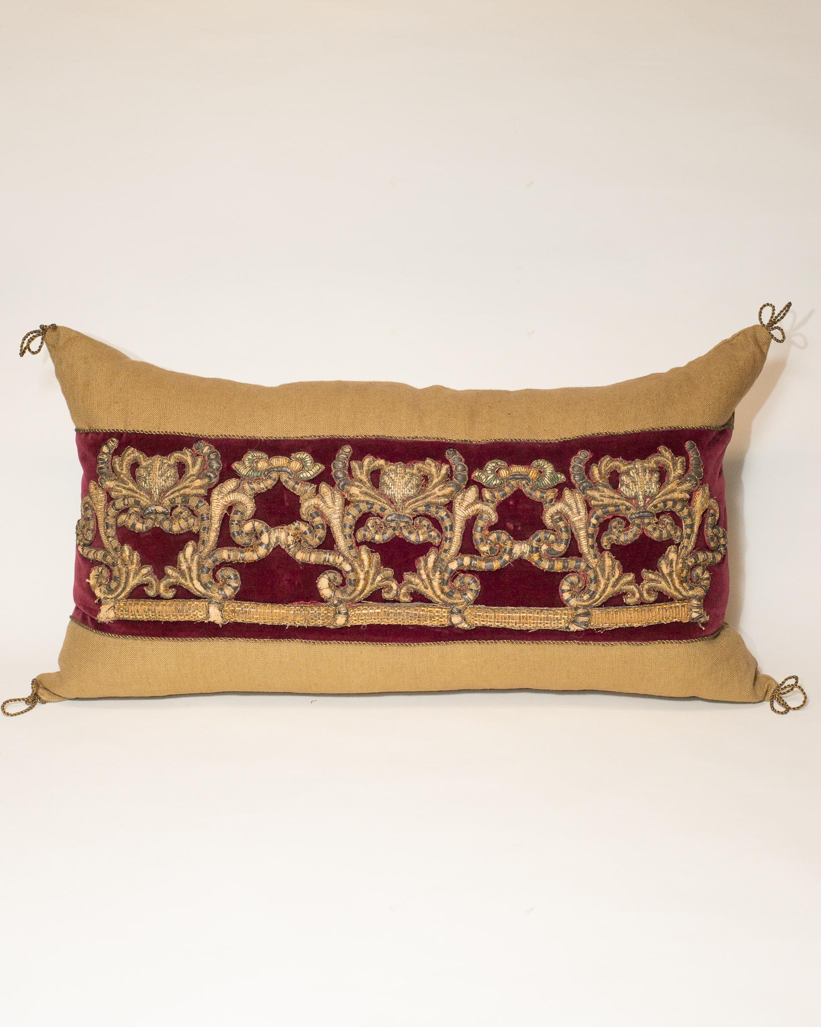 A large beige linen pillow with burgundy velvet and antique metallic embroidery.