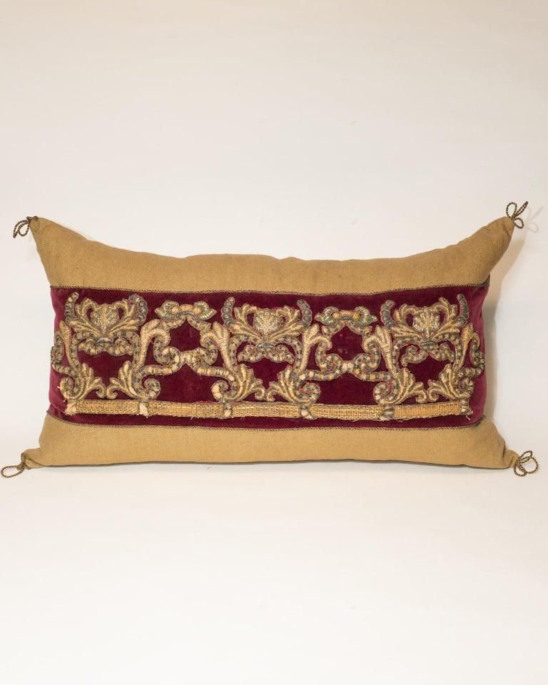 A large beige linen pillow with burgundy velvet and antique metallic embroidery.