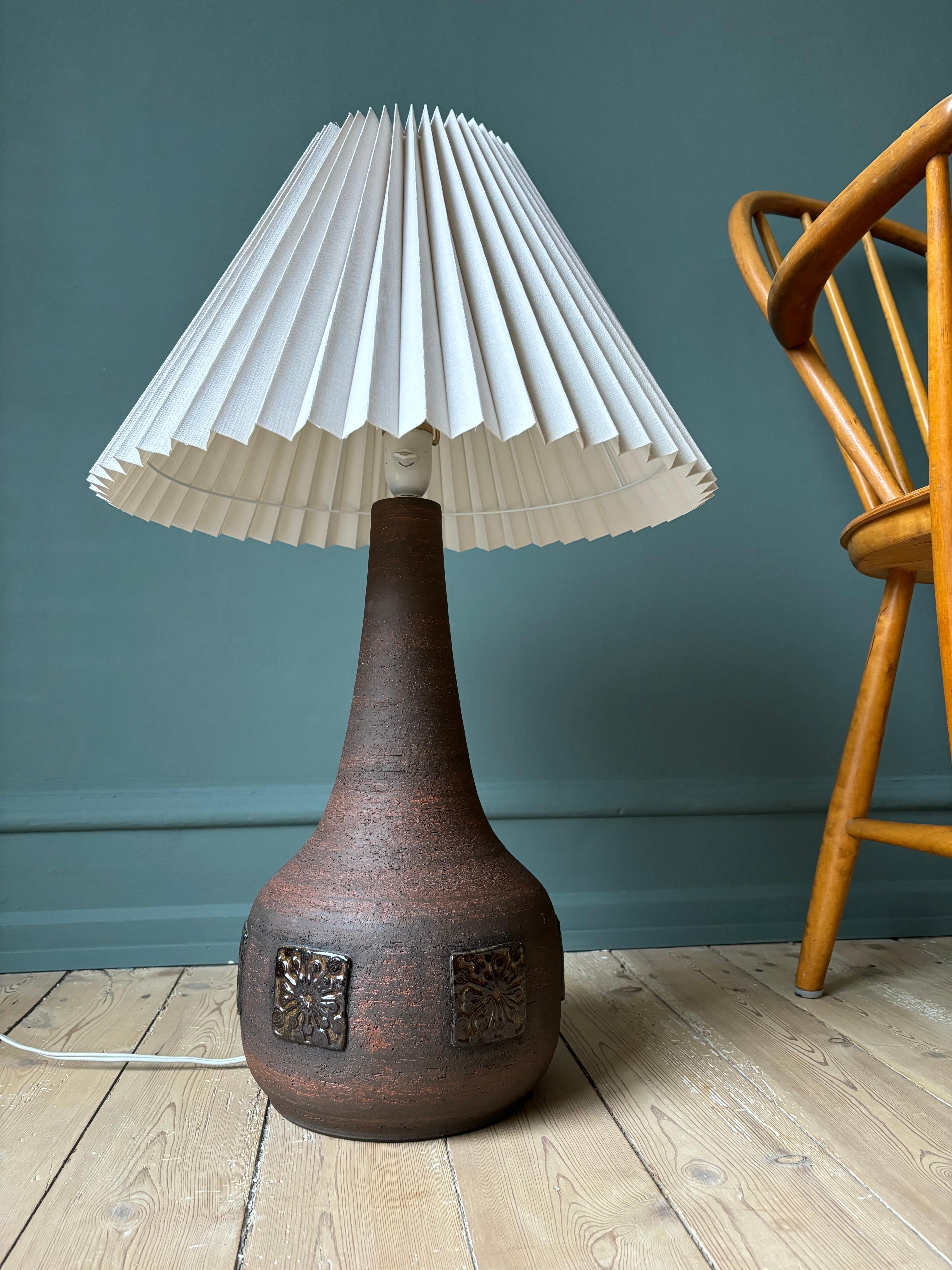 Large handmade modern brutalist stoneware lamp by Belka Stentøj in the 1960s. Raw and unglazed brown chamotte clay material with glazed squares of stylized floral decorations around the large belly. A tall rustic piece that can be used as a table