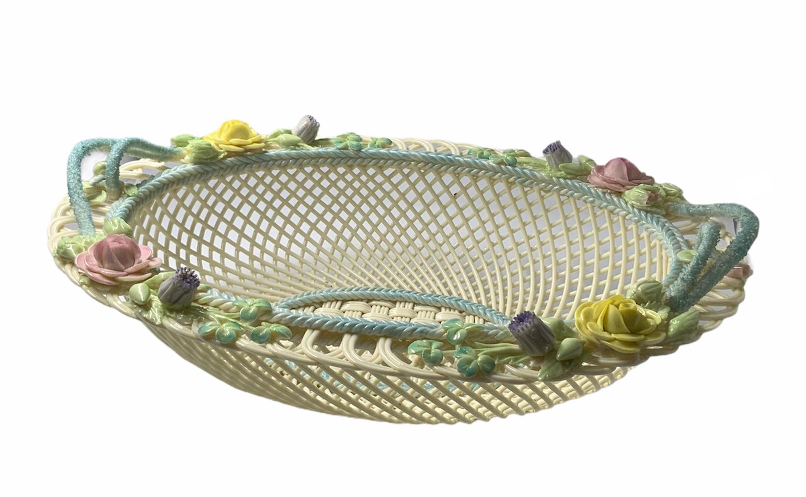 Large delicate oval woven Porcelain basket decorated with a light turquoise braided rim. Alternated large yellow and pink open roses and buds adorn the border together with shamrock branches. Double turquoise ropes Porcelain handles are in each