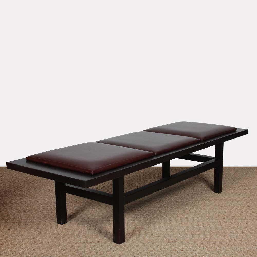 This large bench is in black wood and burgundy leather. It is a late 20th century work. The three seats are removable. This vintage piece is in good original condition.
