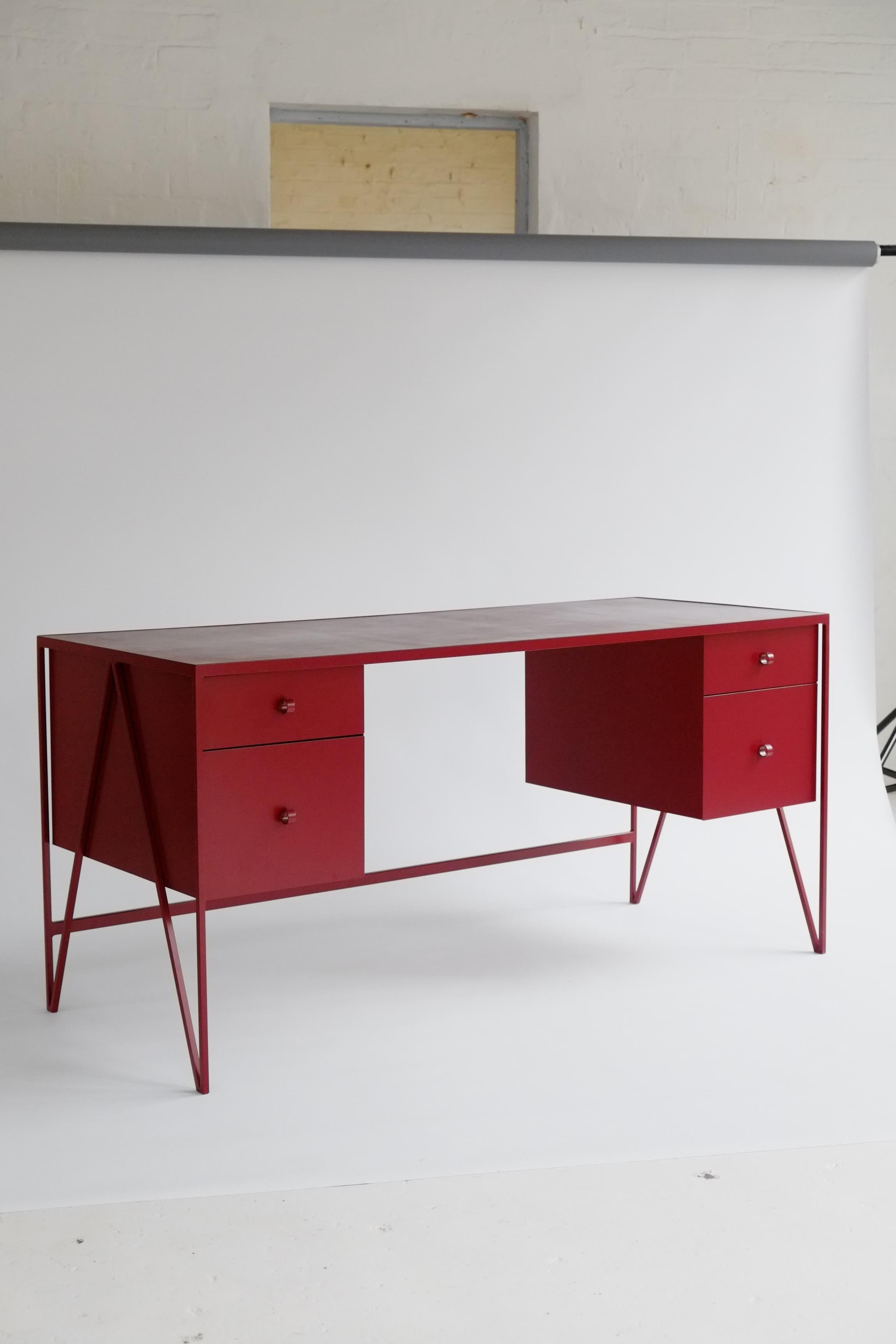 This large burgandy color study desk is made with a powder coated steel frame and a beautiful natural linoleum top made out of linseed oil. This modern minimal desk has four steel drawers suspended underneath the tabletop and Loop handles for pulls.