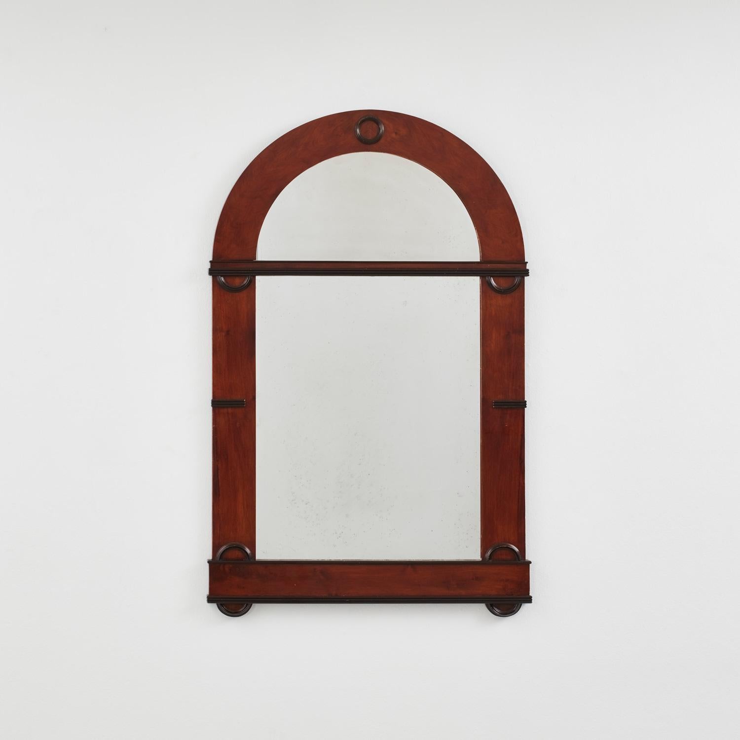 An imposing arched mirror in the Biedermeier style that flourished in central Europe in the first half of the 19th century. Its restrained ornamentation is typical of the movement, which heralded Art Deco in geometric forms and simplified classic