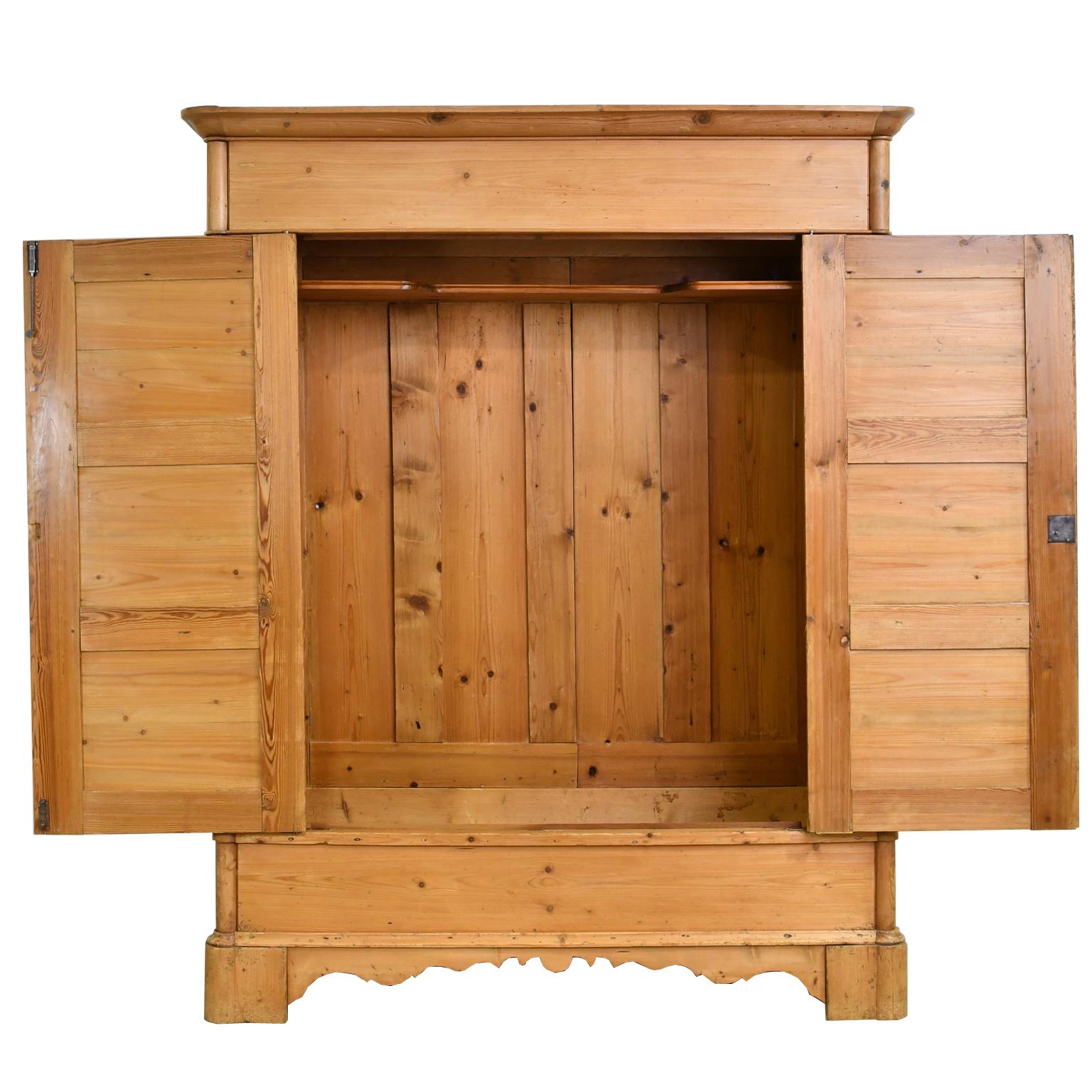 A beautiful large North German armoire in light, honey-colored pine with two doors with three raised panels on each, paneled sides and bracket feet with scalloped apron. Doors open on offset pivot hinges allowing easy access to the armoire's