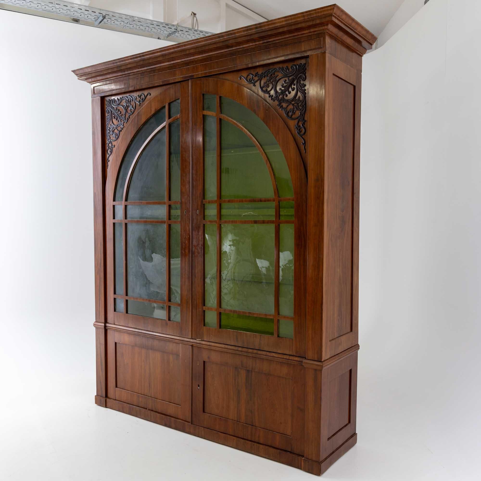 Large library cabinet with a two-door lower section and a two-door upper section with glazed and arched doors and carved vine decoration in the spandrels. The cornice is profiled several times. The inside of the cabinet is painted green and fitted