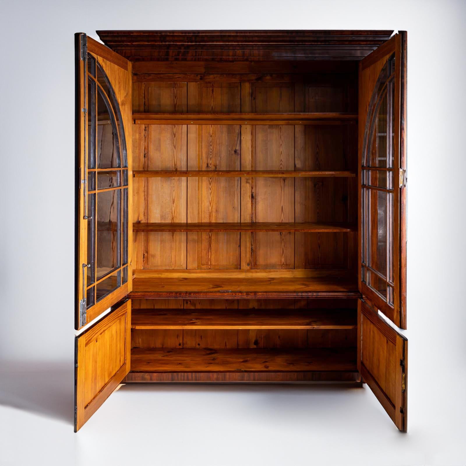 Large library cabinet with a two-door lower section and a two-door upper section with glazed and arched doors and carved vine decoration in the spandrels. The cornice is profiled several times. The inside of the cabinet is painted green and fitted