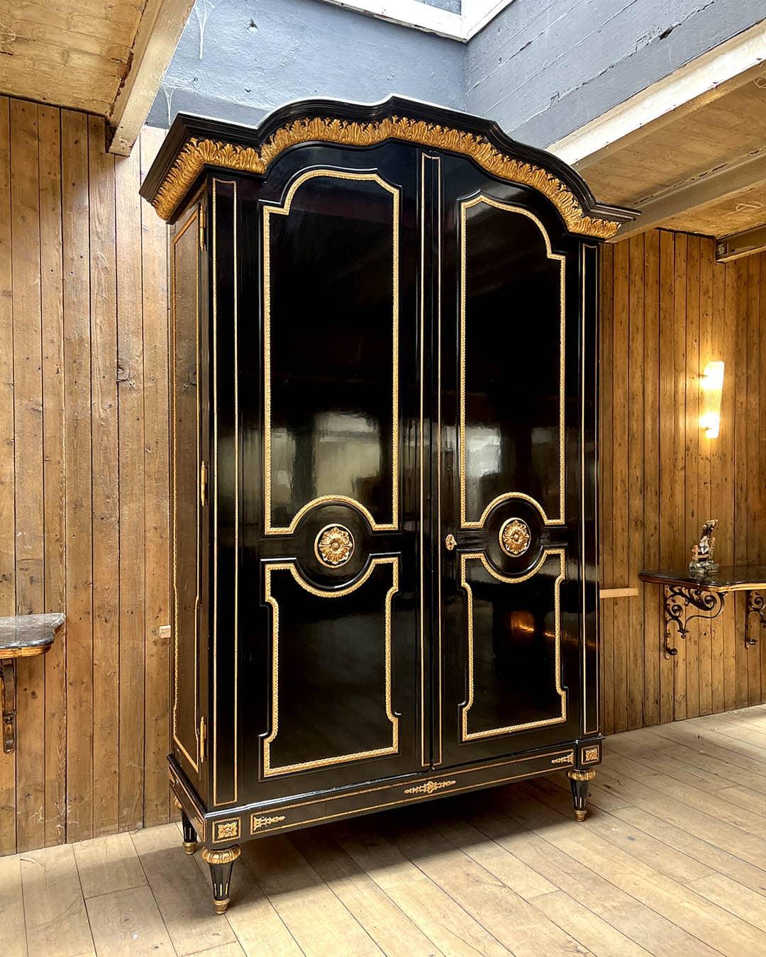 Impressionante e riccamente decorato armadio in legno annerito con dettagli in legno dorato, realizzato in stile Luigi XVI. L'imponente presenza architettonica è accentuata dal cornicione ad arco ornato da foglie d'acanto dorate finemente