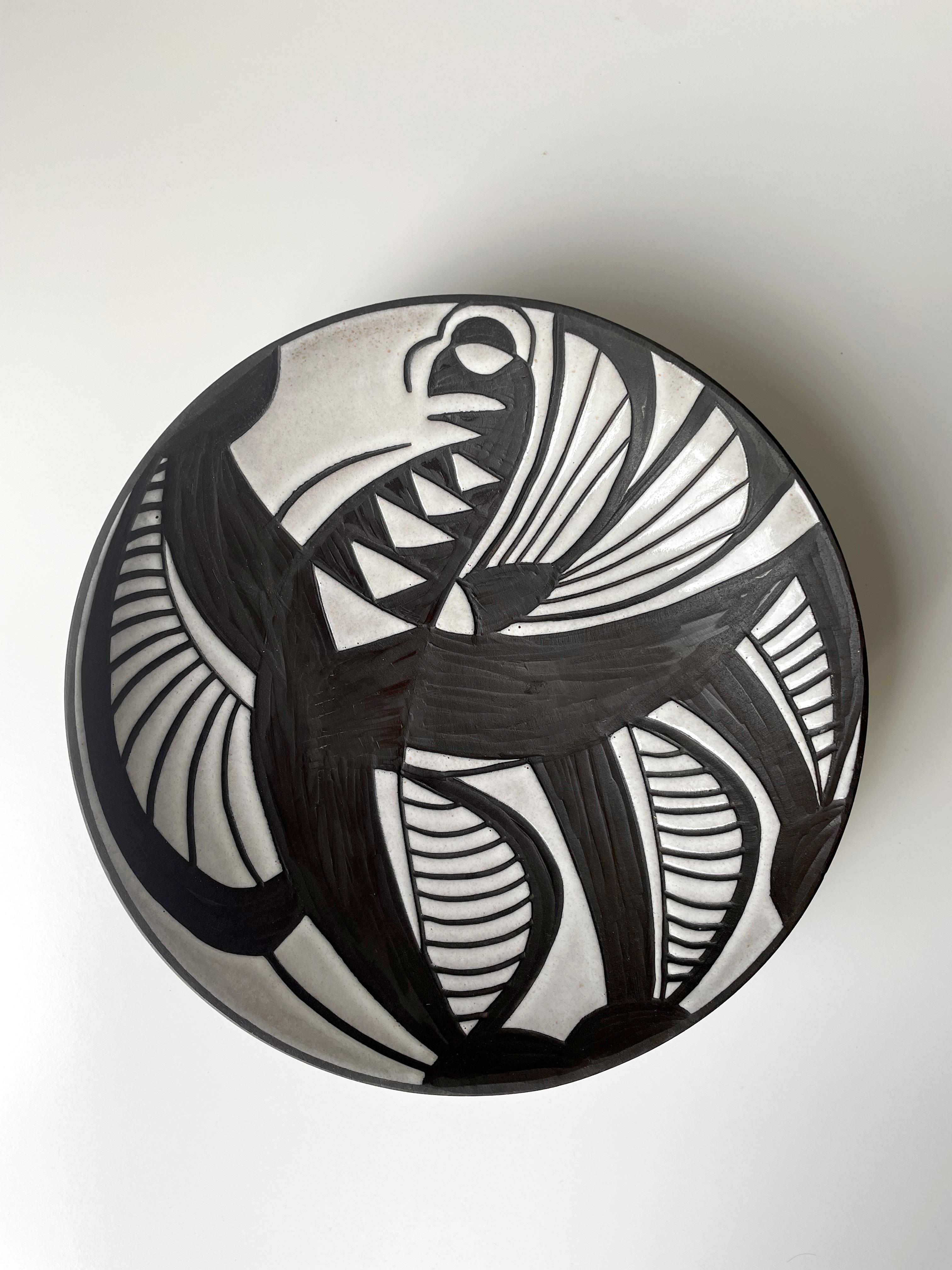 Danish modernist decorative plate / wall decoration / centerpiece with strong graphic decor from the Tribal Harlekin series by ceramic artist Marianne Starck (1931-2007). Shiny bone white glaze with hand-carved sgraffito graphic lines and patterns