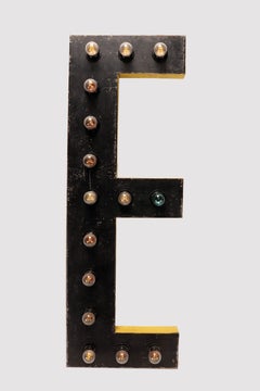 Gran letra E de hojalata negra y amarilla iluminada por bombillas. EEUU 1930.