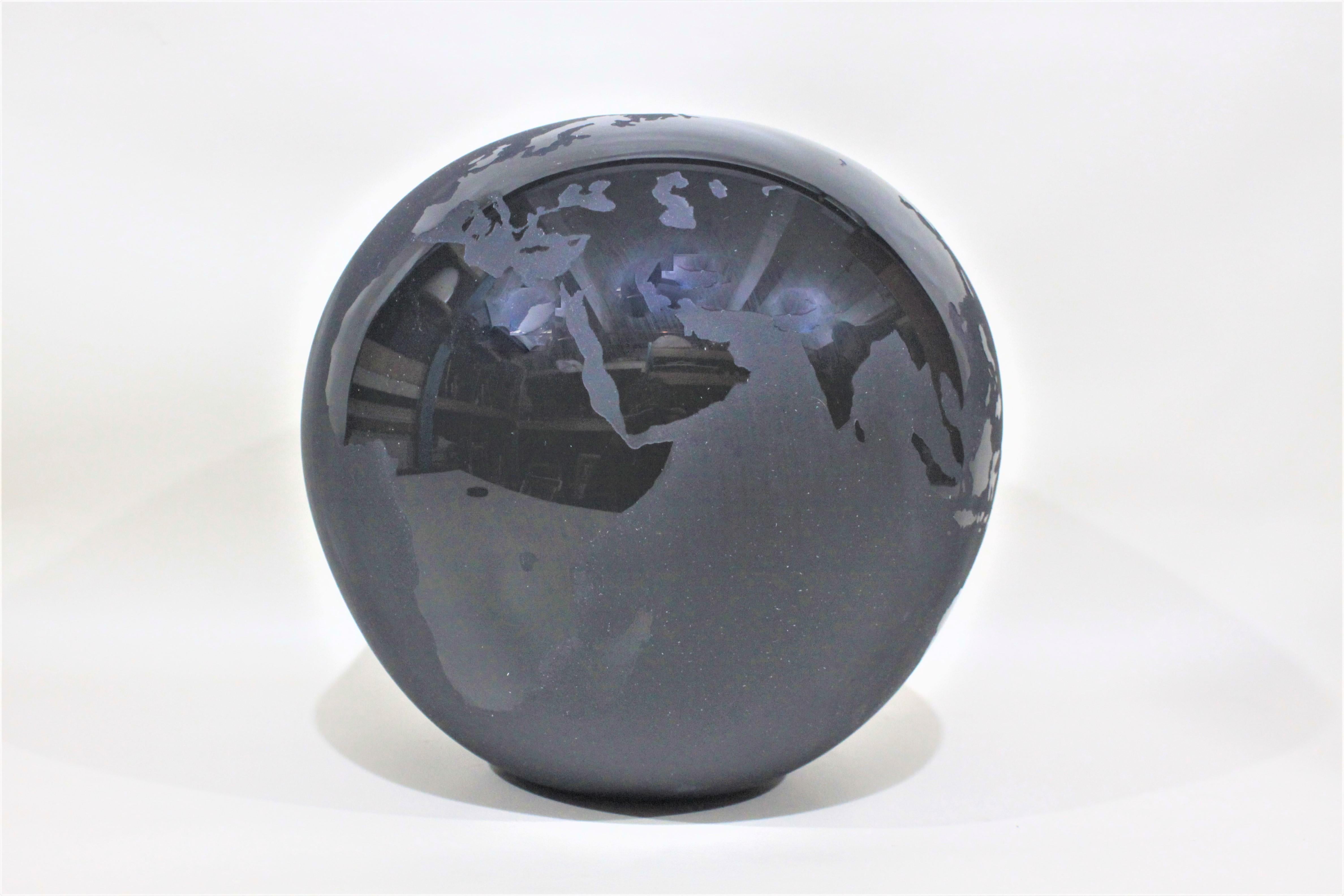 This contemporary artist signed black glass vase was likely done between 1980-1990 and depicts a stylized rendering of the world globe. Unfortunately the artist's signature is illegible. This black art glass vase is etched resulting in a contrast of
