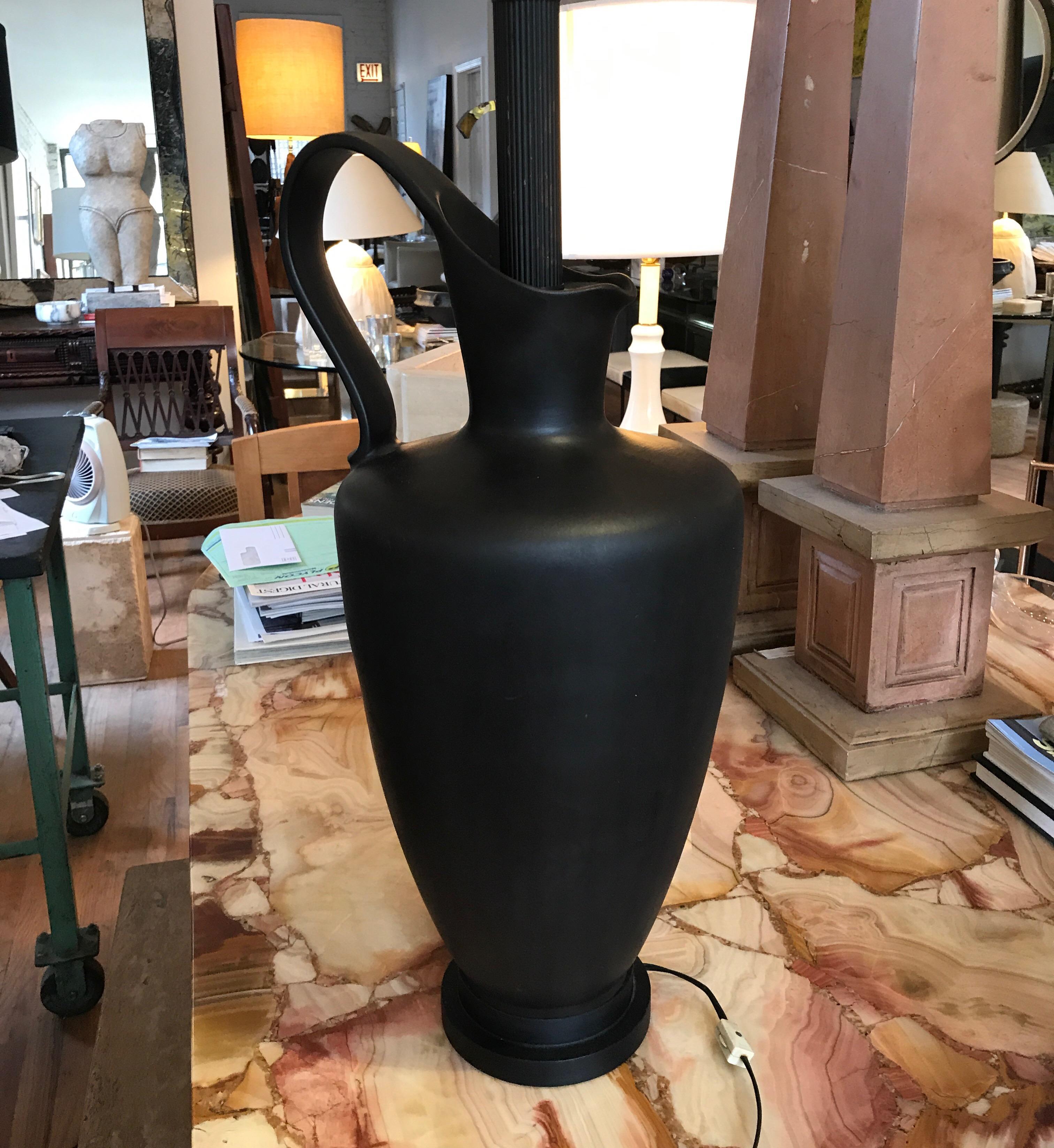 Monumental midcentury black ceramic lamp. The lamp is a Classic Greek form pitcher or Oenochoai. 
Its undecorated black matte form would compliment period or contemporary interiors.
The measurement is to the top of the finial.
The pitcher