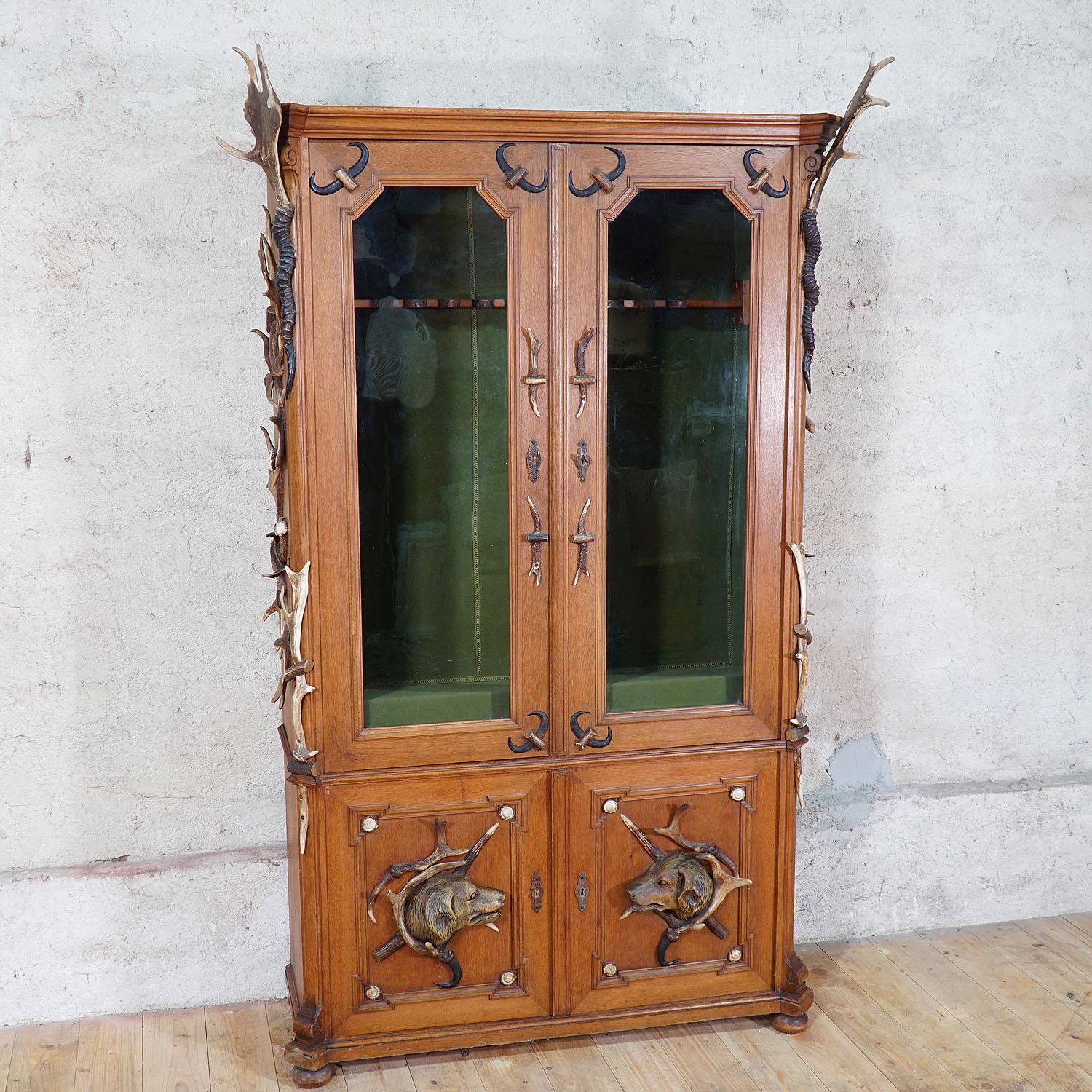 A large antique oak wood gun cabinet decorated with several original antlers from the deer, the fallow deer, antelope and chamois. Elaborately manufactured with many details like the covers of the locks which are made made of antler. Booth lower