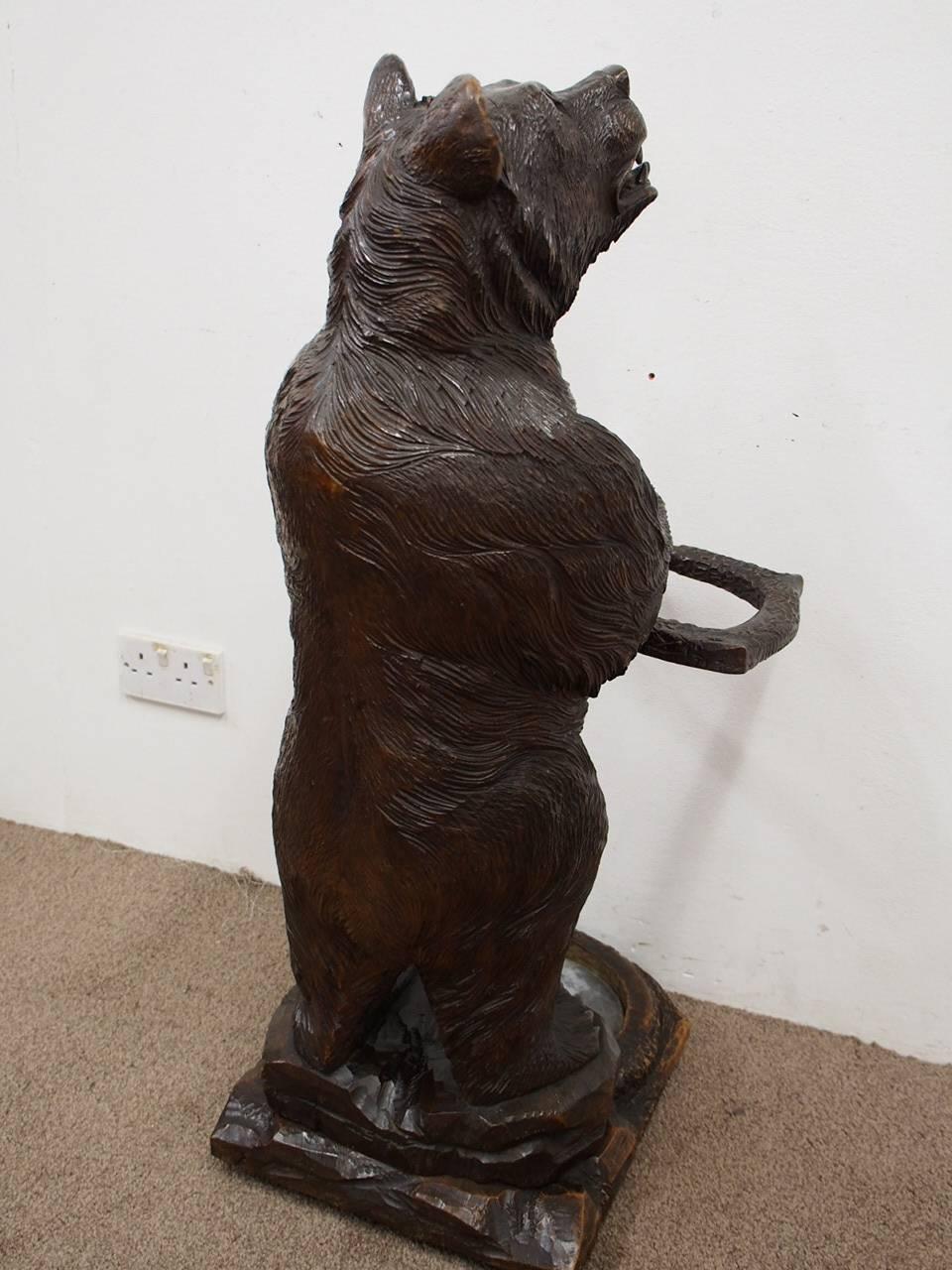Large Black Forest carved bear stick stand, circa 1880. With realistically carved glass eyes, and the paws clasp a bracket in the form of braches for retaining the walking sticks. It stands on a rustic base and beneath is a shaped drip tray.