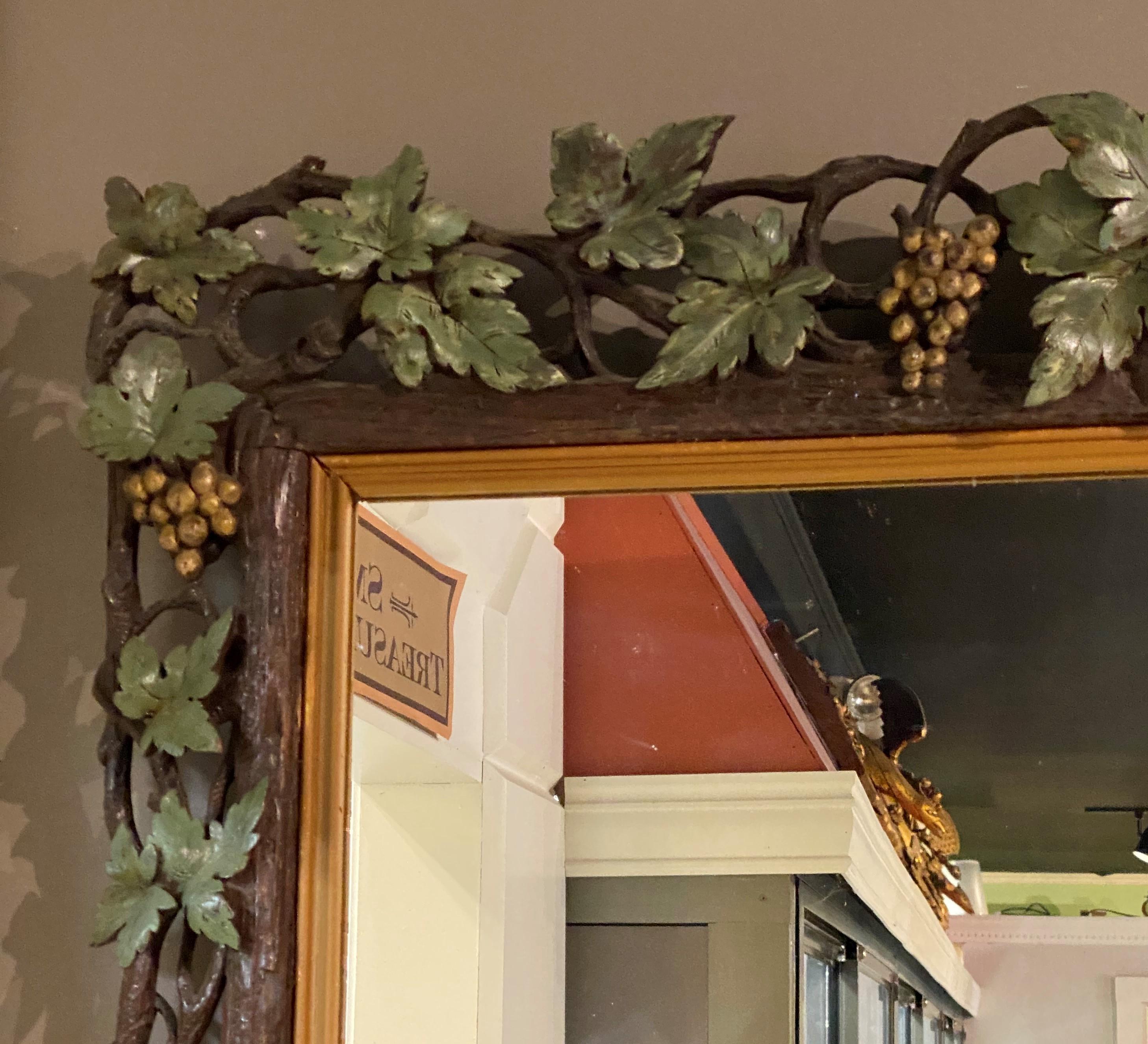A fine large rectangular wall mirror with Blackforest reticulated wooden carved frame, probably walnut, with grapevine motif, hand painted in brown, green, and gold with gilt molded inset. Dates to the late 19th or early 20th century in very good