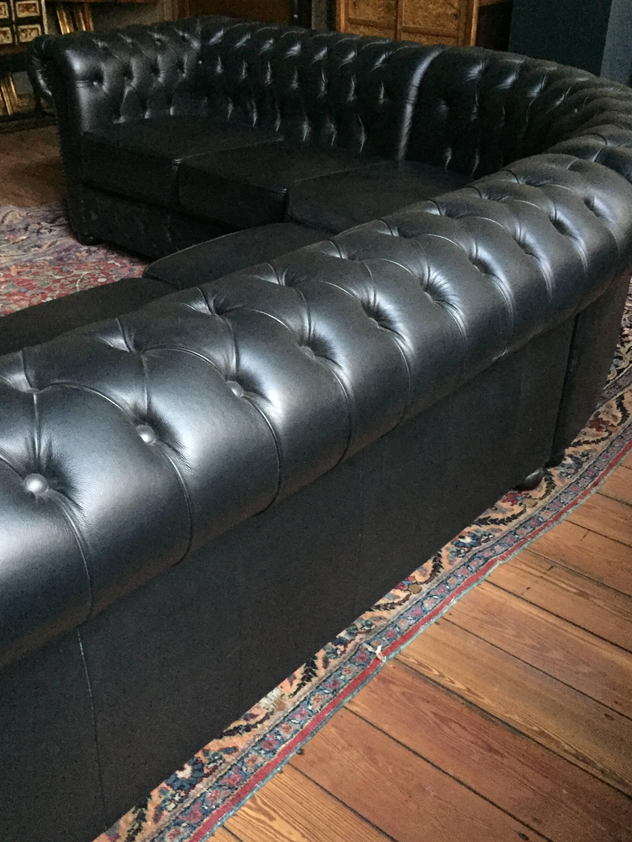 English Rochester Chesterfield sectional sofa in a two-seat x three-seat L shape. Black leather with brass nailhead detailing and wood bun feet. In absolutely excellent condition; purchased about 20 years ago to be used in a Belgian Parliament