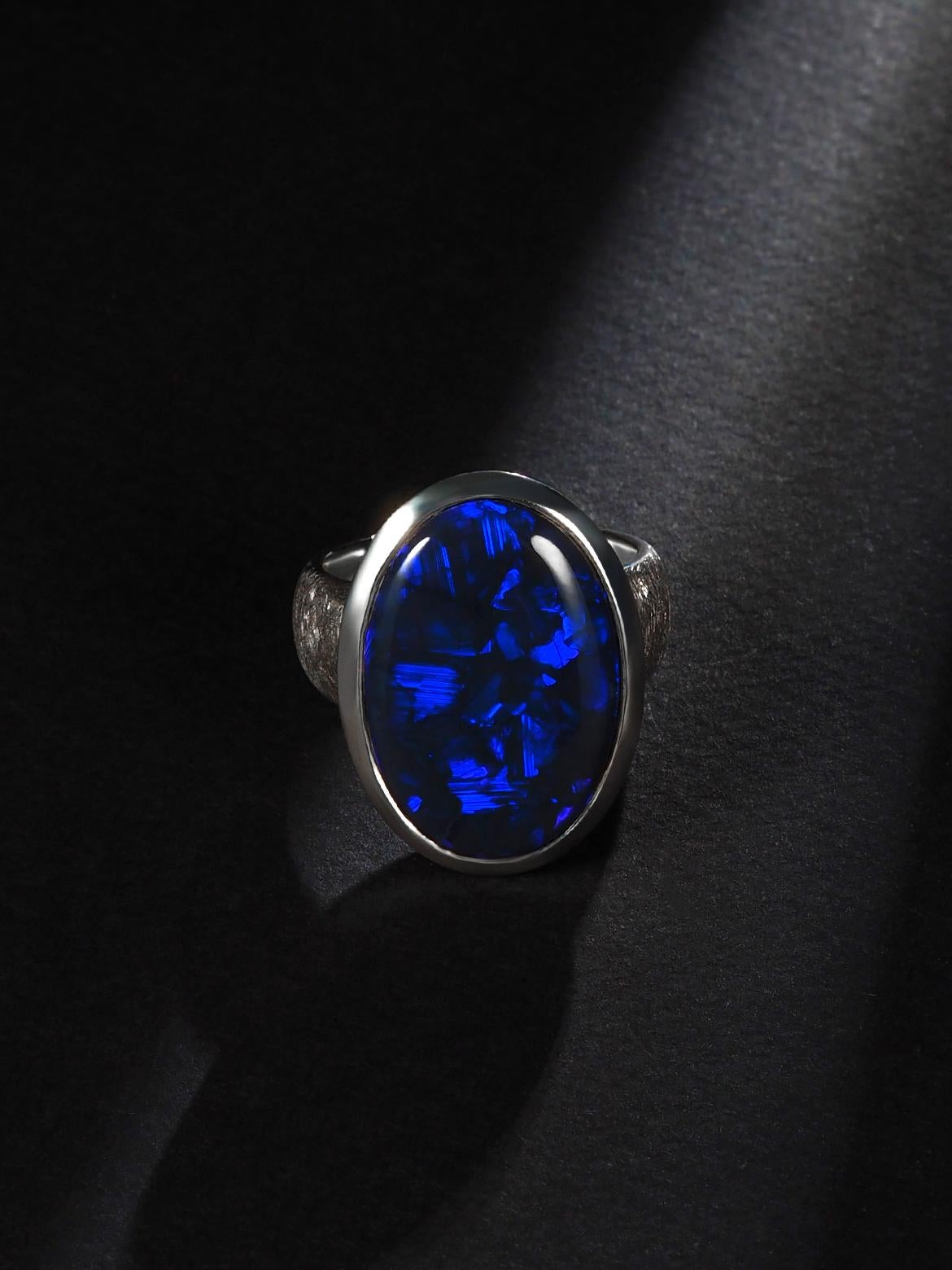A stunning and unique piece, this large black opal ring showcases the captivating beauty of Australian opals. The opal displays a mesmerizing play of colors, with deep hues of neon blue shining through against a dark background.

The opal is
