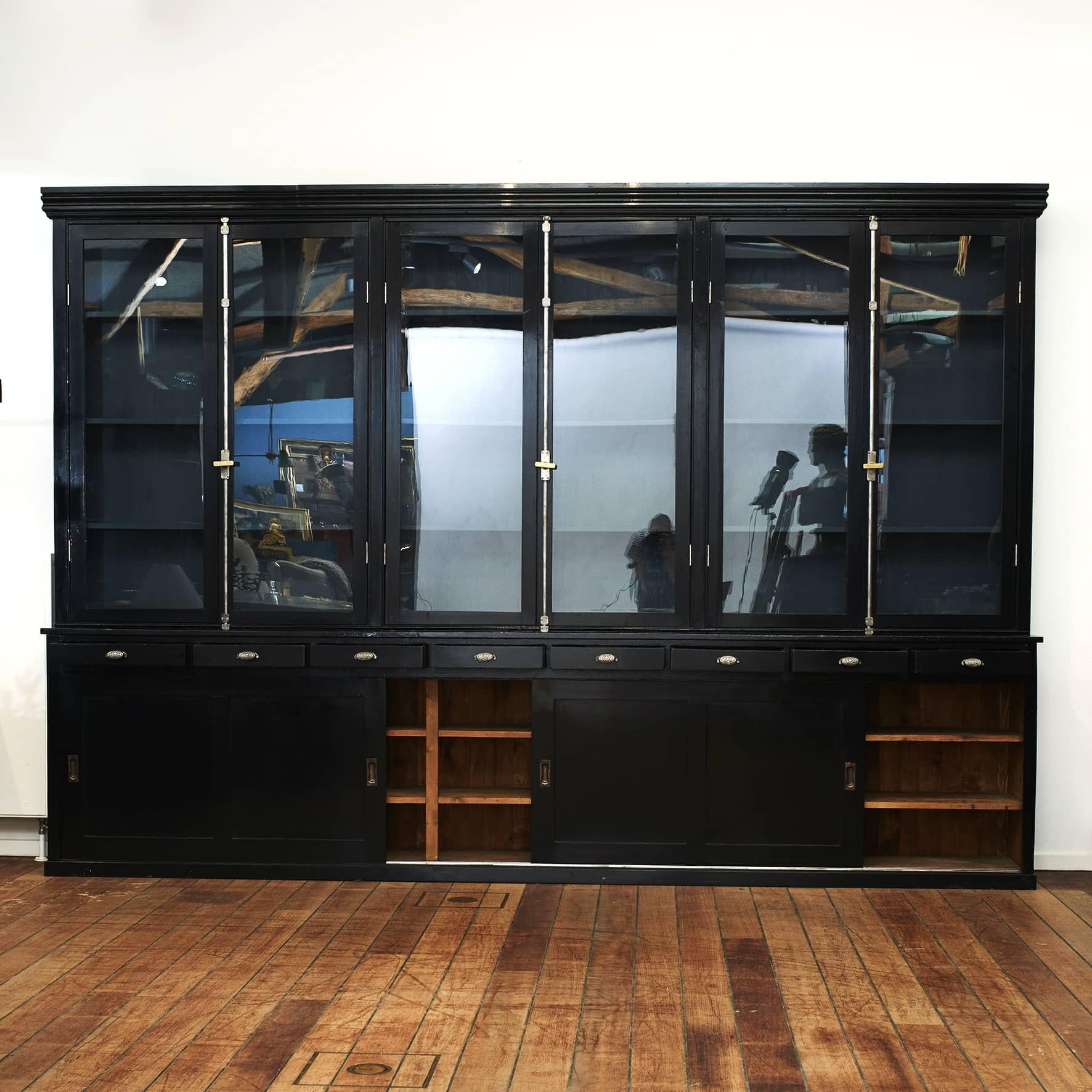 Outstanding large ebonized wood mercantile shop display cabinet. In two parts.
The top section having 3 glass doors that open up to shelves for ample storage, with metal and brass locking mechanism.
The lower section has 8 drawers above 3 sliding