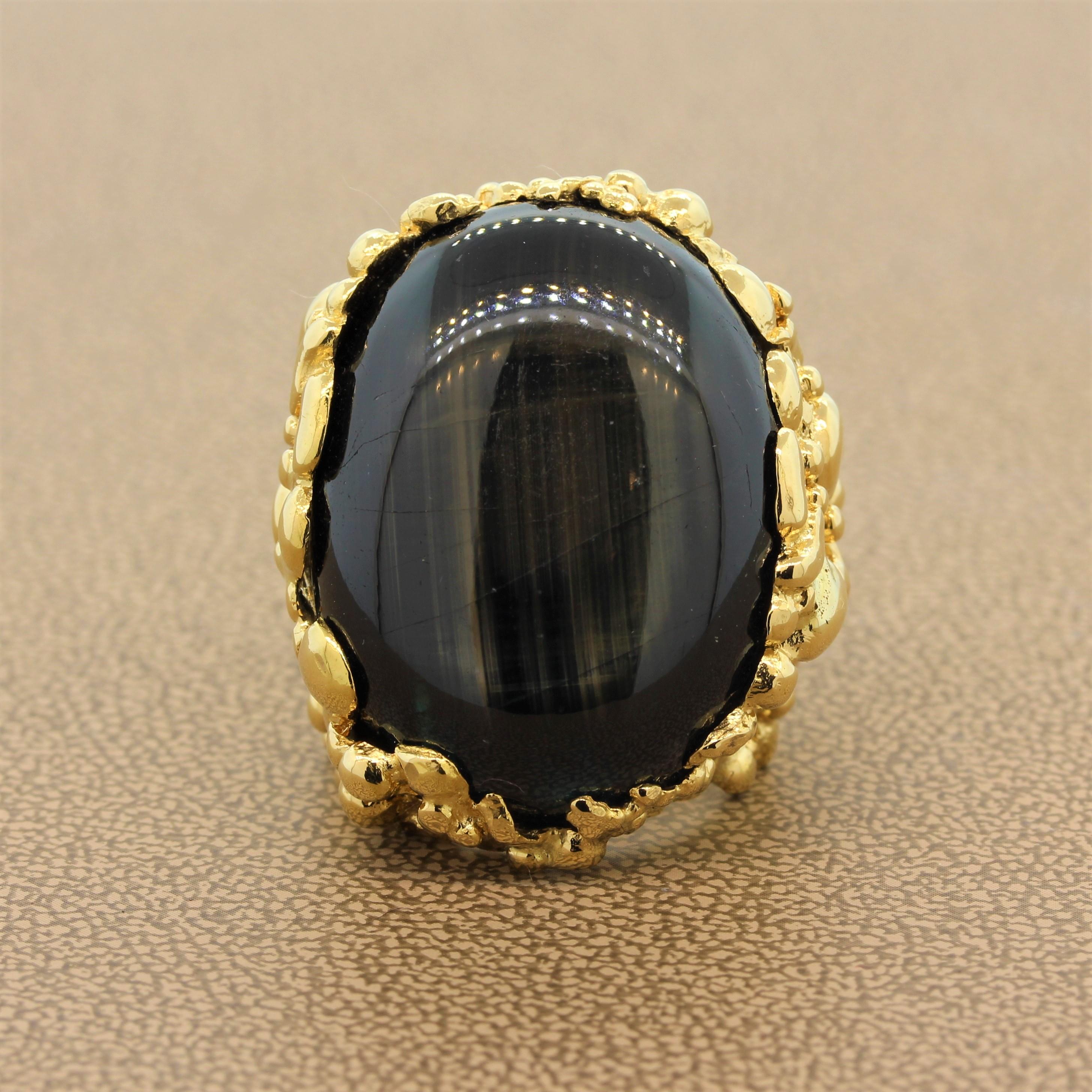 An impressive ring featuring an approximately 100 carat black star sapphire with strong asterism. The oval shaped cabochon is set in an 18K yellow gold filigree setting contrasting with the dark color of the sapphire.

Ring Size 5.25 (Sizable)
