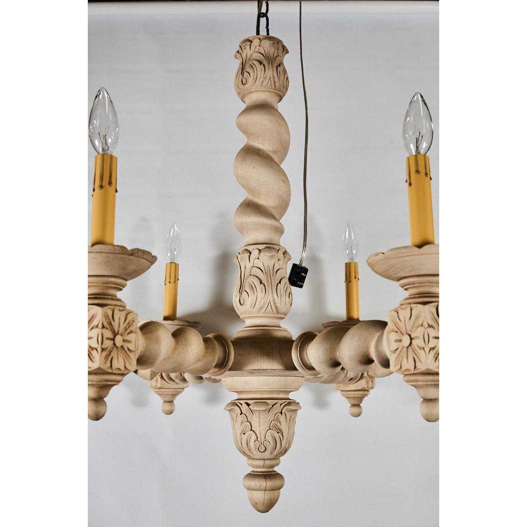 This highly carved chandelier is thought to be French and from the earlier part of the 20th century. We have bleached the finish to give the piece an updated look. It has an extended wooden central turned barley twist column and a brass ceiling
