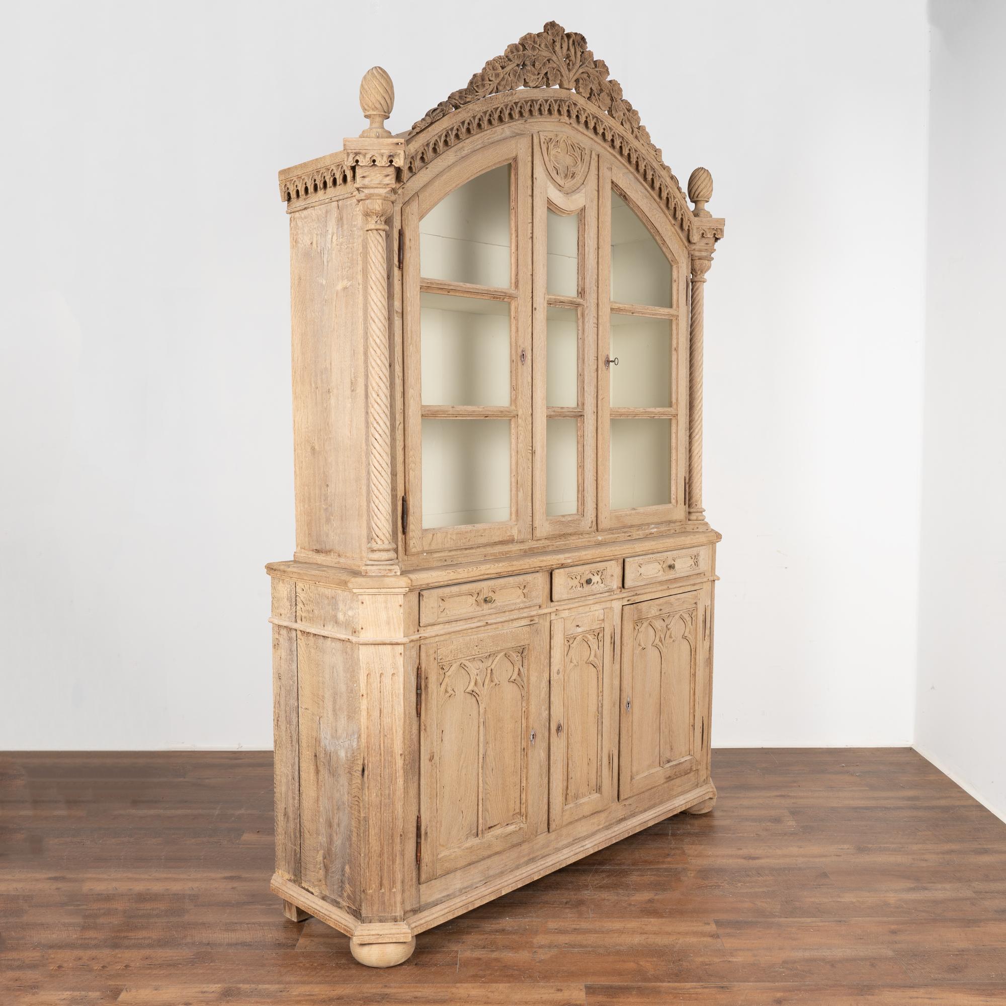 This large bleached oak bookcase has intricate details such as the gothic trim that accents the crown and panel doors in addition to the dramatic turned columns, finials and more.
The interior of the cabinet has been painted, allowing for great