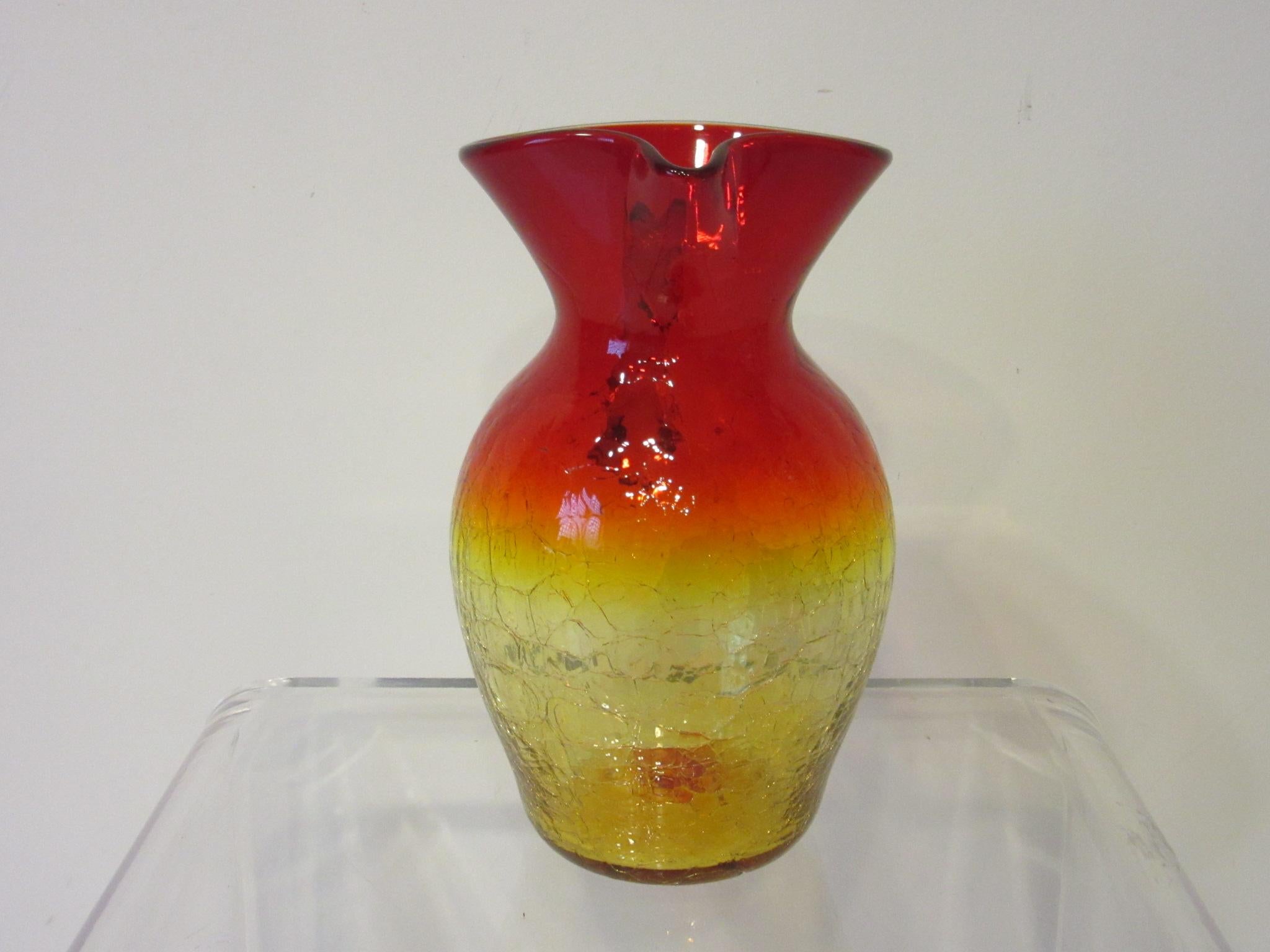 A large hand blown art glass pitcher in tangerine and ruby with the crackle textured pattern produced under the Blenko Glass company designed by Wayne Husted.