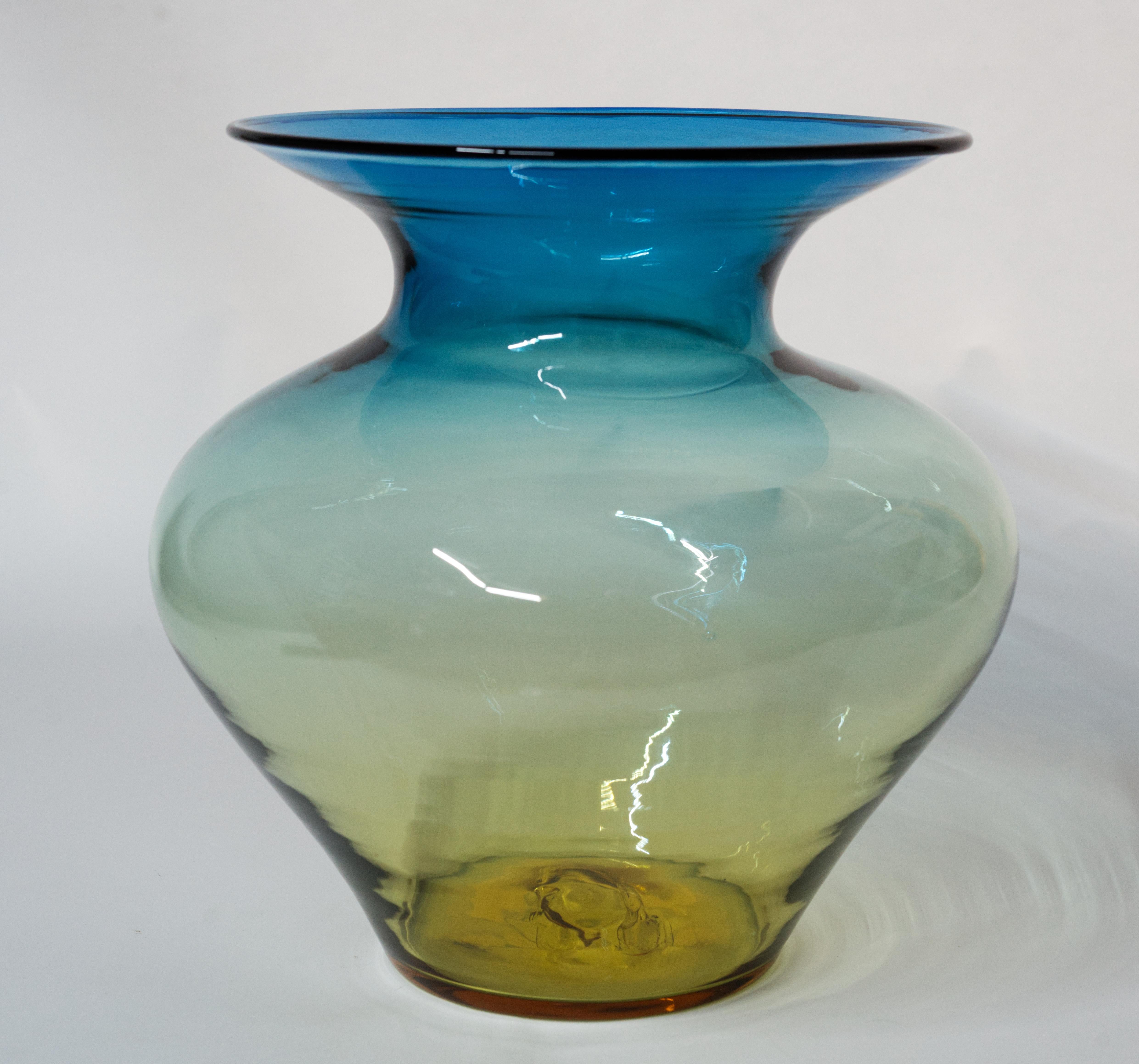  Large Blenko Glass Vase is hand blown in Desert Green color, with ombré color changes from a deep green to amber/yellow.

Desert green color is made by taking a gather of blue Cobalt glass and encasing it in yellow Topaz, but leaving a very thick
