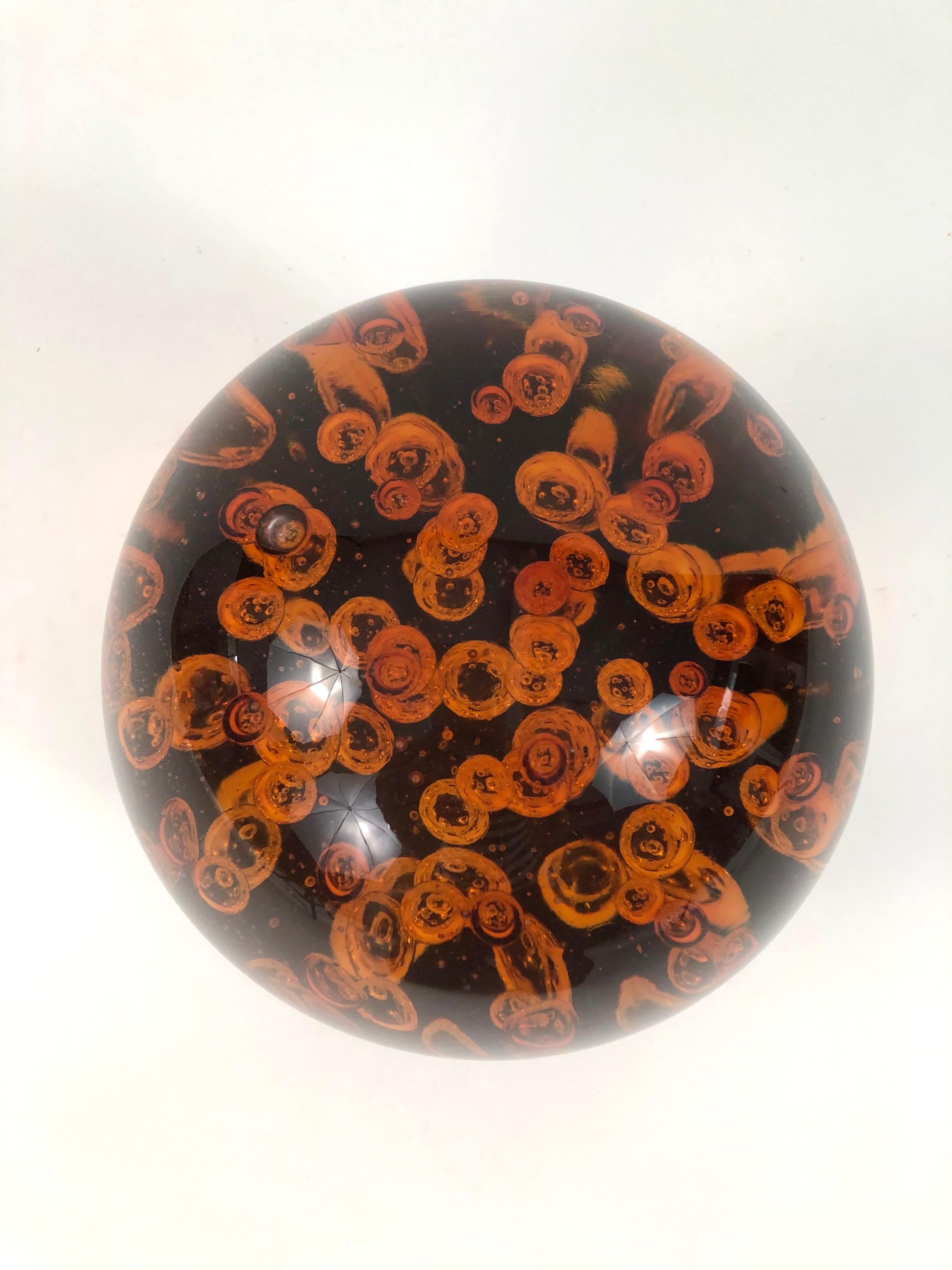 A large vintage amber blown glass sphere, with large bubbles inside, heavy weight and richly colored, resting on a slate (?) veneered square stand. Wonderful table decoration or doorstop. Heavy weight and rich color.

Measures: Height on stand