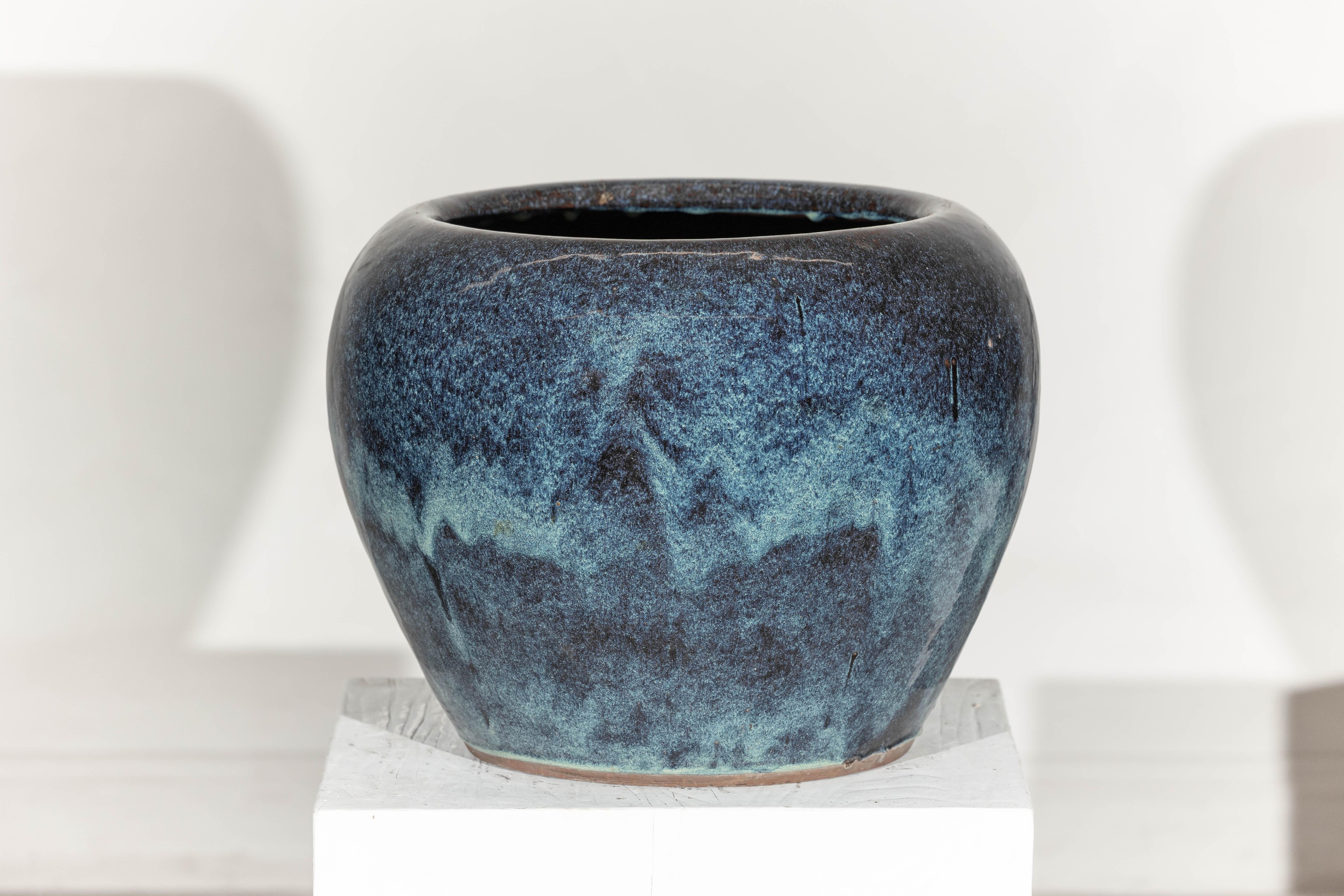 Avec son riche mélange de bleu profond, de brun discret et de tons aquatiques lavés sur une silhouette arrondie, cette grande jardinière ajoute une touche picturale à tout décor. Sa glaçure vive passe de l'indigo de minuit à l'aqua mousseux, avec
